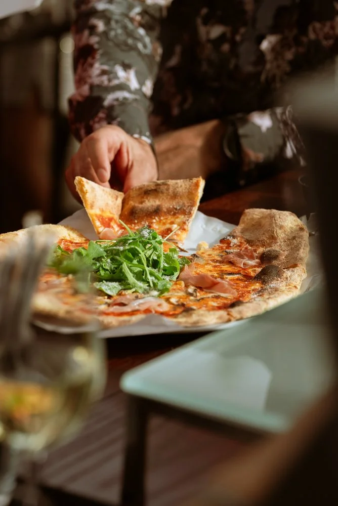 Person reaching for a slice of pizza with arugula salad on the side on a plate.