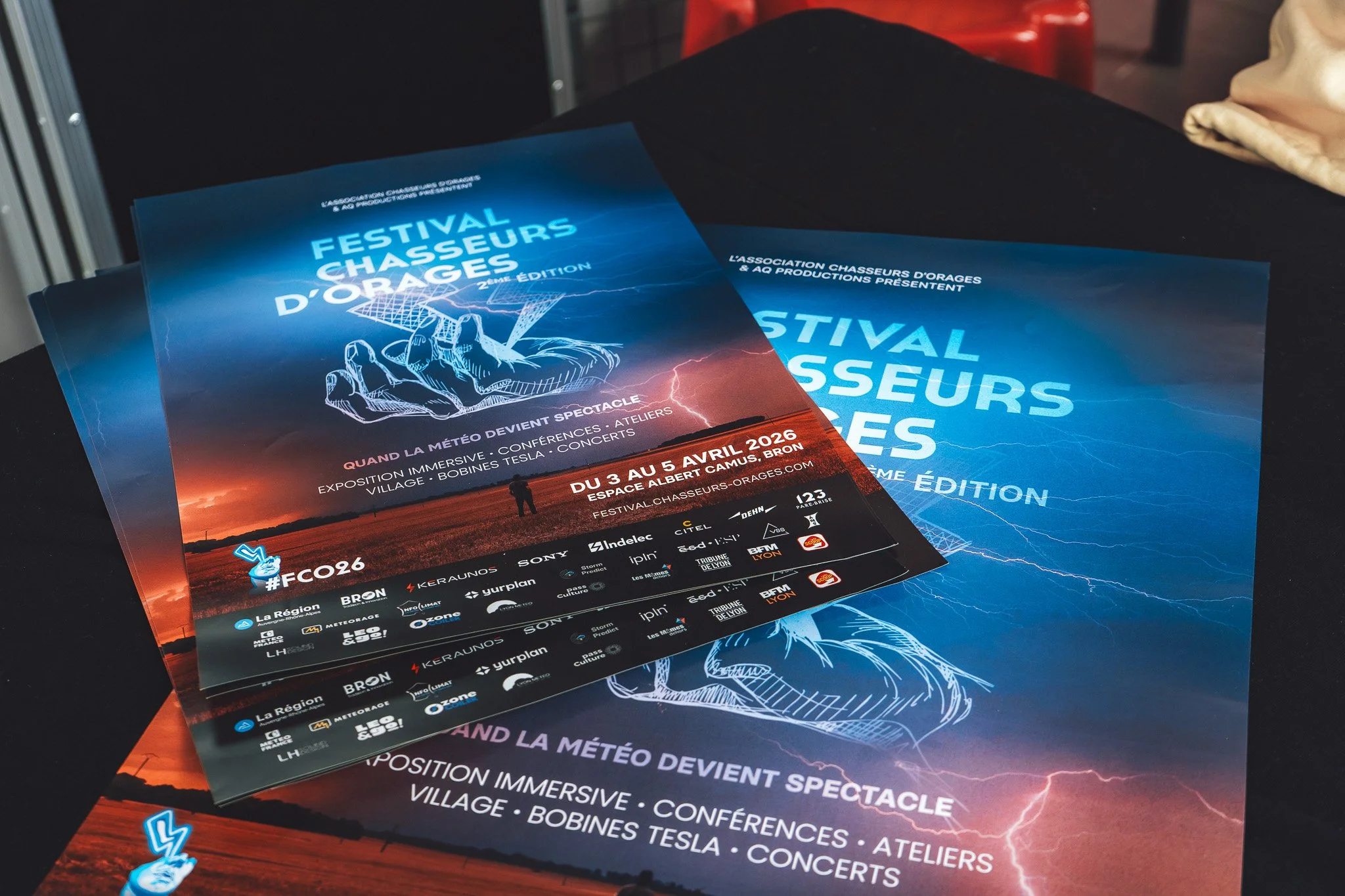Flyers promotionnels pour le festival chasseurs d'orages 2026, avec une image d'orage, des éclairs et un paysage de coucher de soleil, présentant des informations sur l'événement du 3 au 5 avril 2026 à Éspace Albert Camus, Bron.