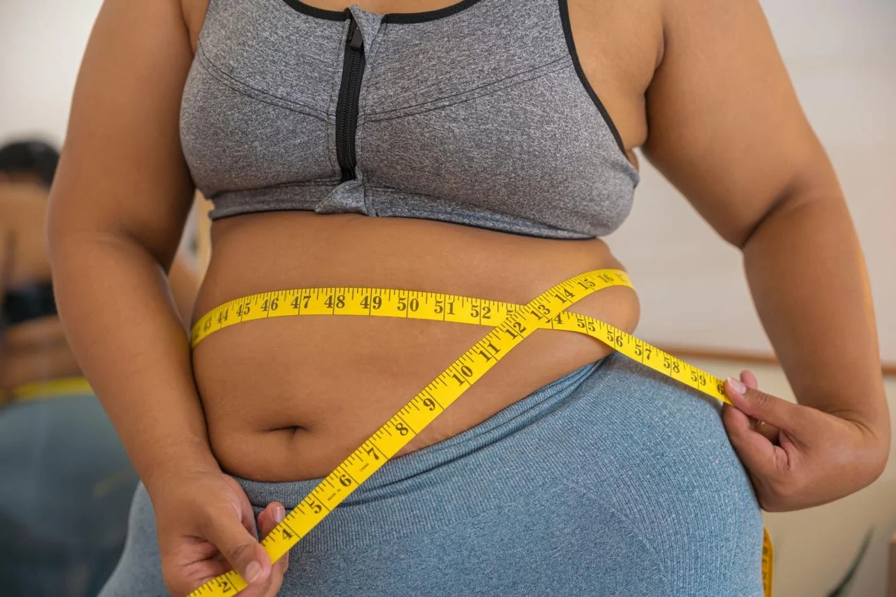 A person measuring their waist with a yellow tape measure.