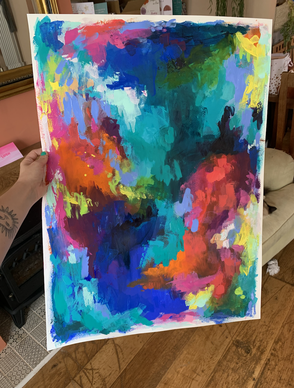 Hand holding a colorful abstract painting with splashes of blue, green, pink, red, purple, yellow, and orange on a canvas