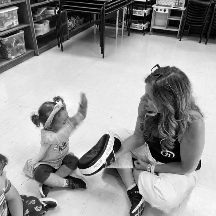 A young girl and an adult woman sitting on the floor in a classroom, engaging in a playful game with a target pad.