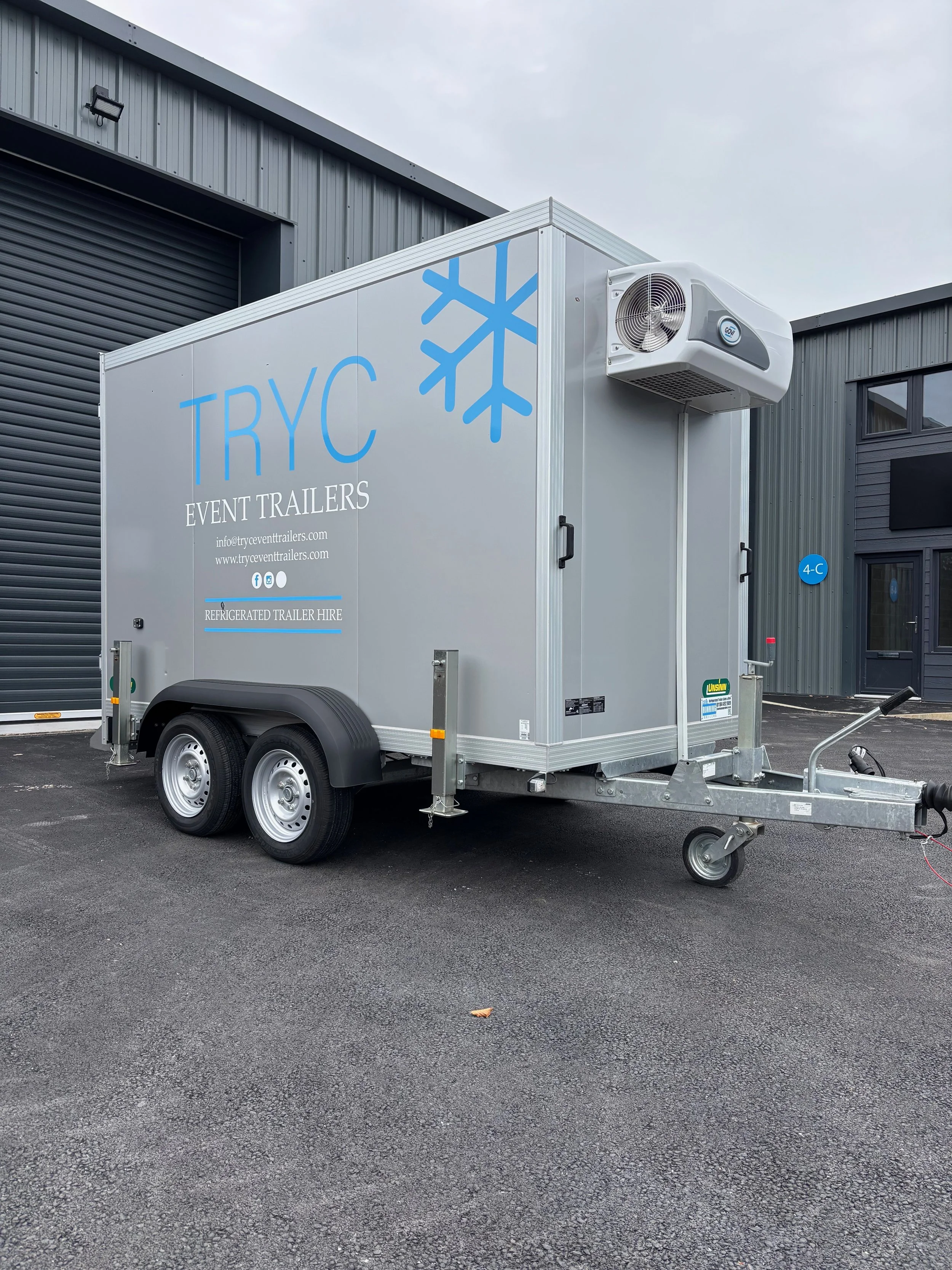 A refrigerated trailer with the branding TRYC Event Trailers, parked outside a commercial building.