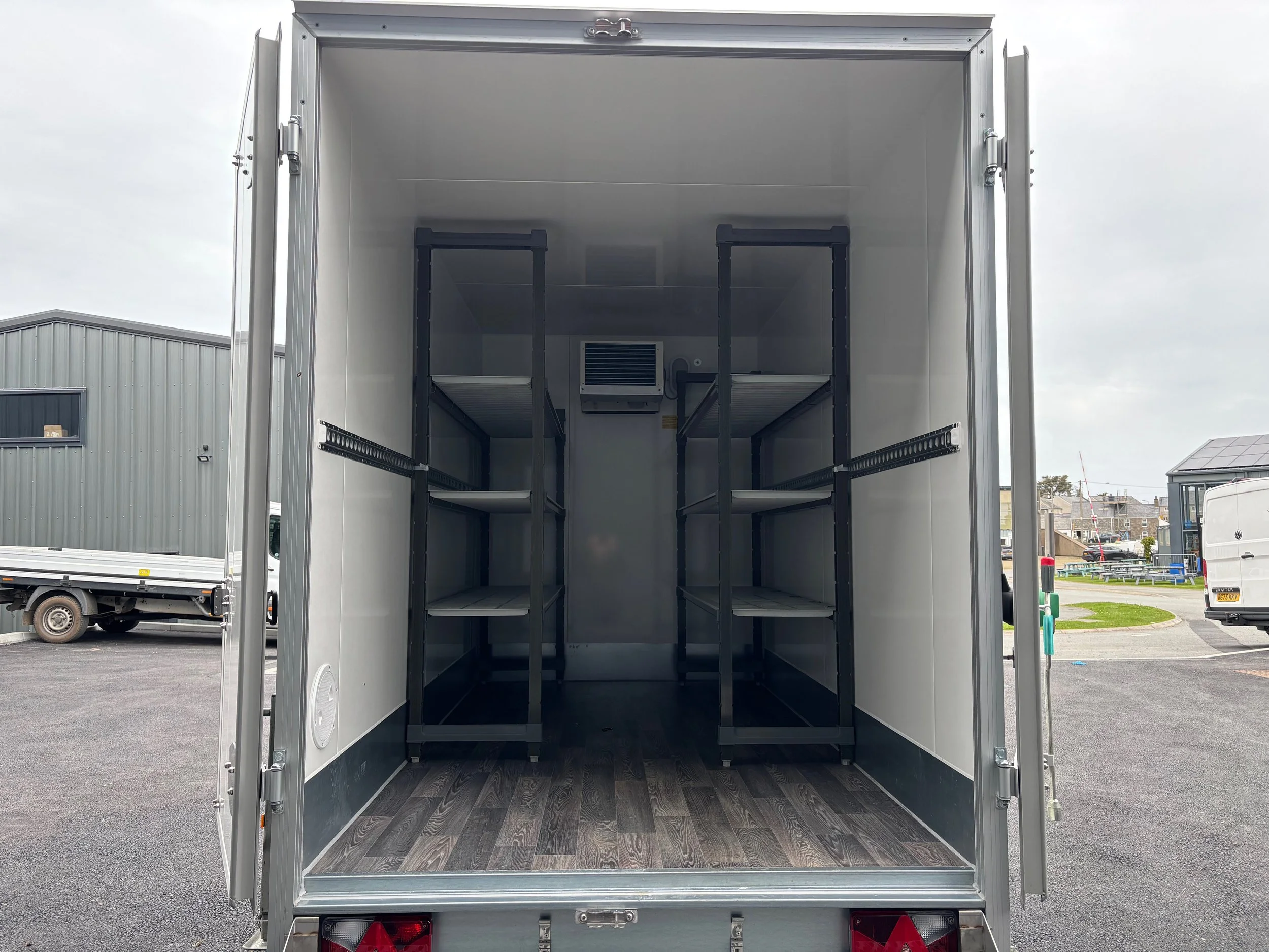 Interior of an empty storage or moving truck with black shelving units and a small vent or air conditioning unit on the back wall.