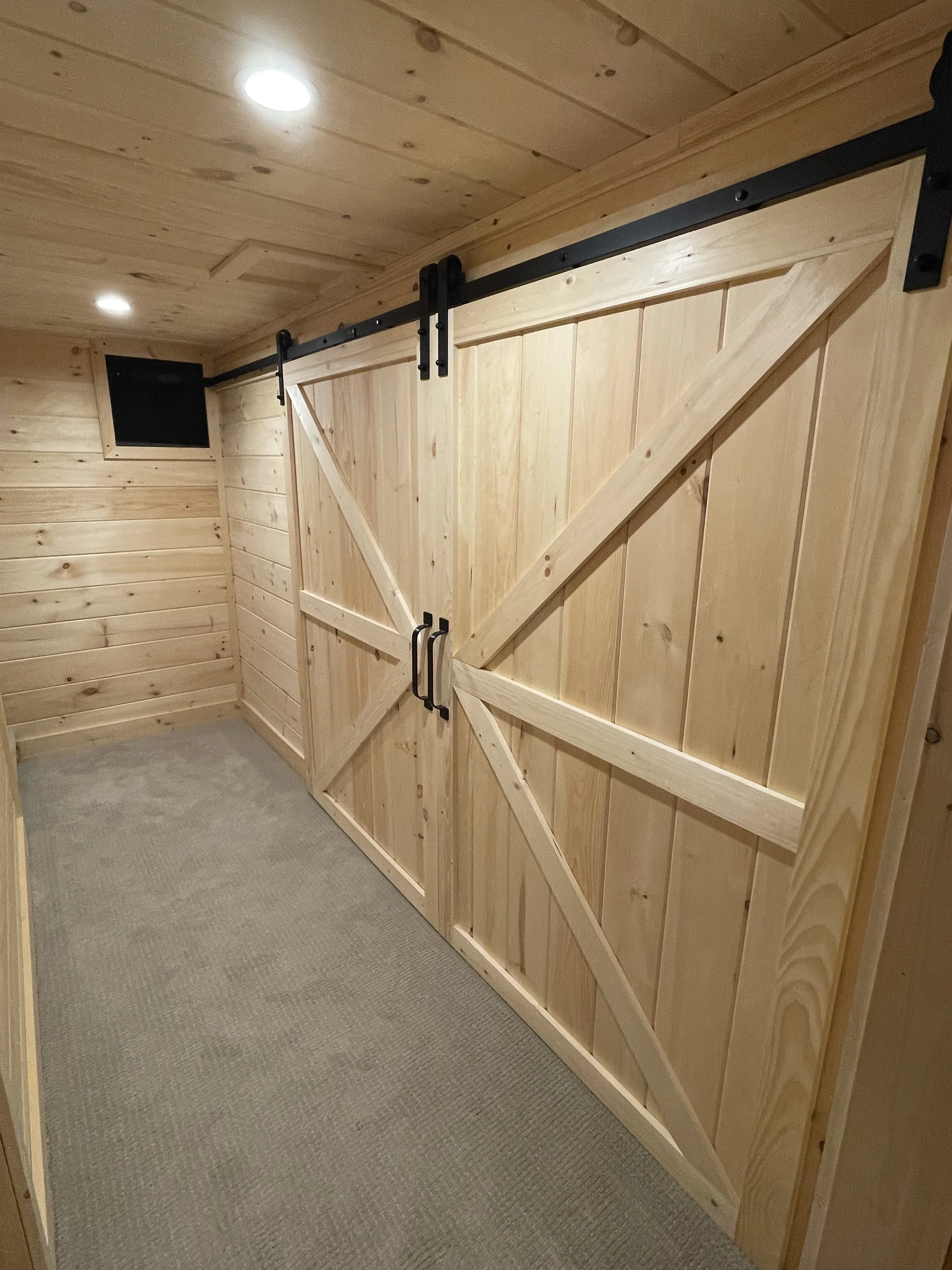 Wooden shed interior with sliding barn doors, wooden walls, ceiling, and carpeted floor.