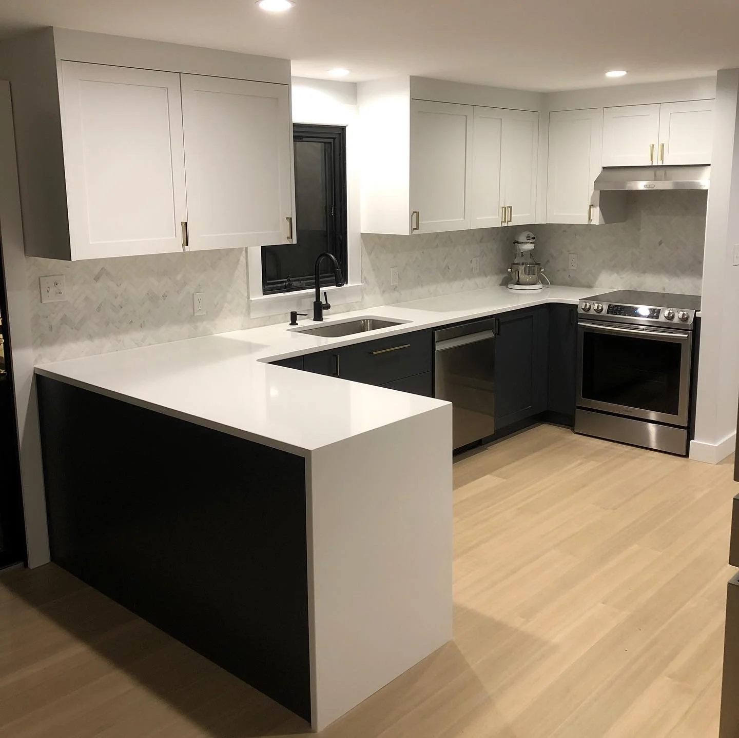 Modern kitchen with white and black cabinets, white countertops, stainless steel appliances, a black faucet, and a small window above the sink.