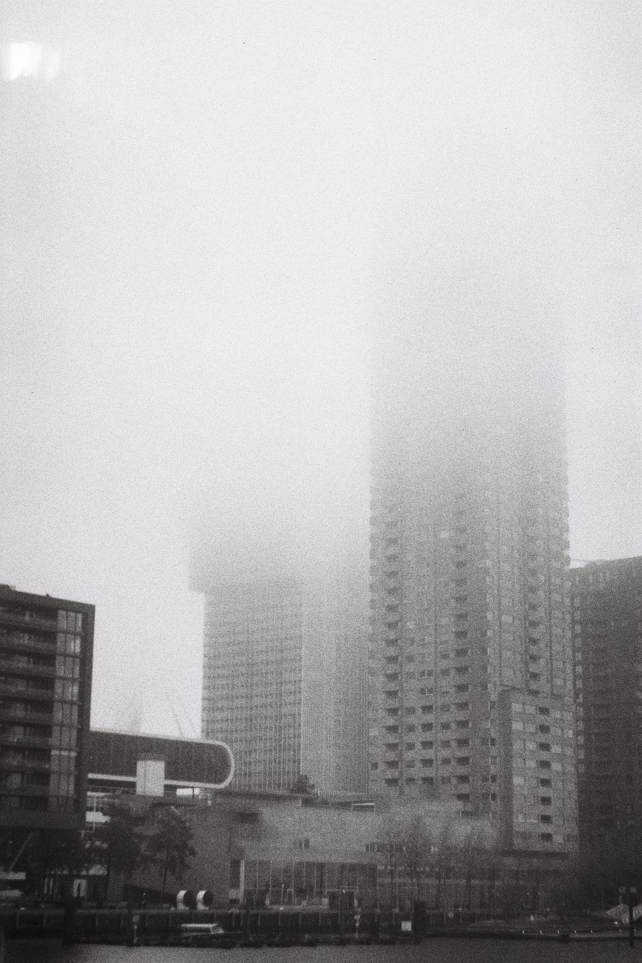 A foggy cityscape with tall modern skyscrapers shrouded in fog, and shorter buildings in foreground.