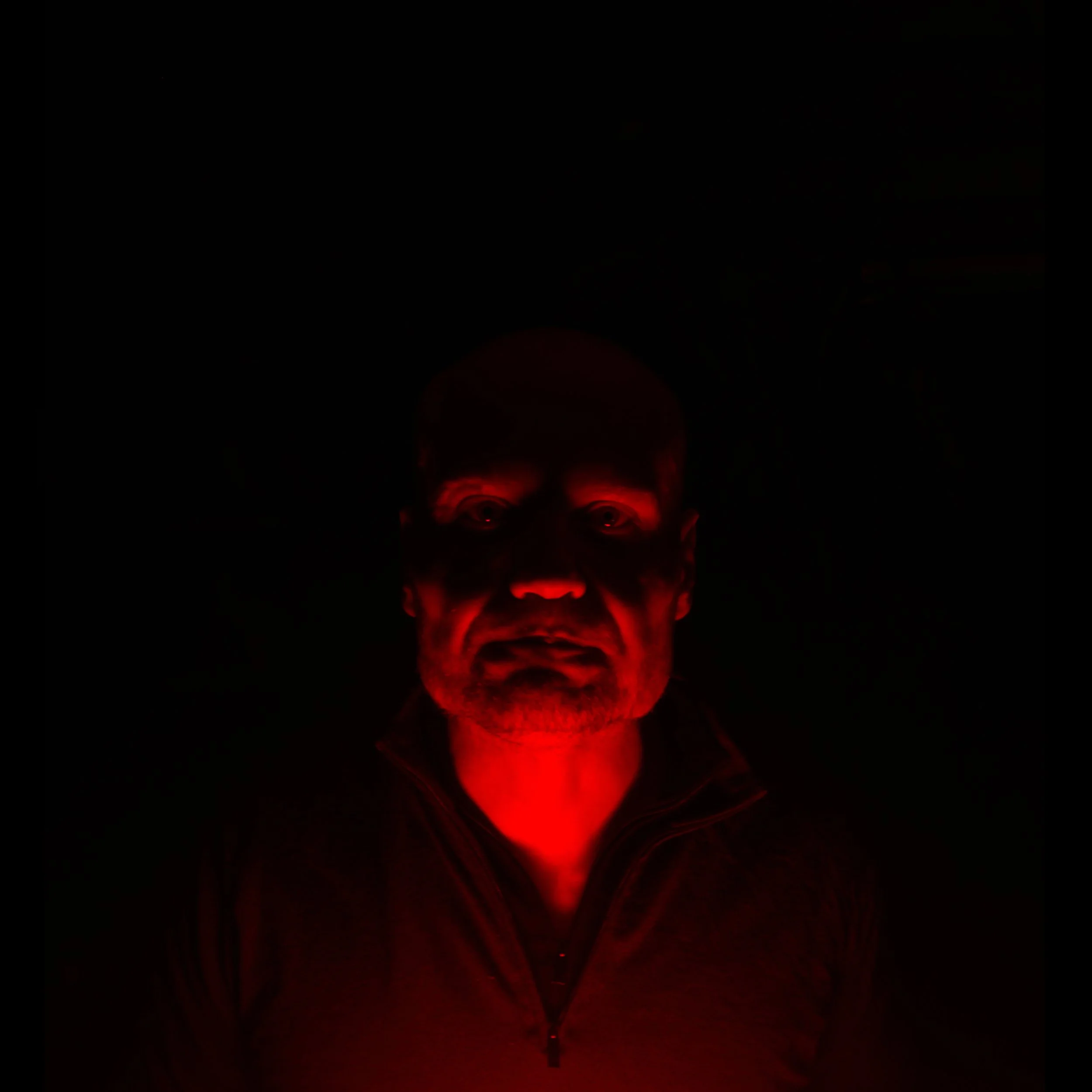A man with a serious expression illuminated by red light in a dark environment