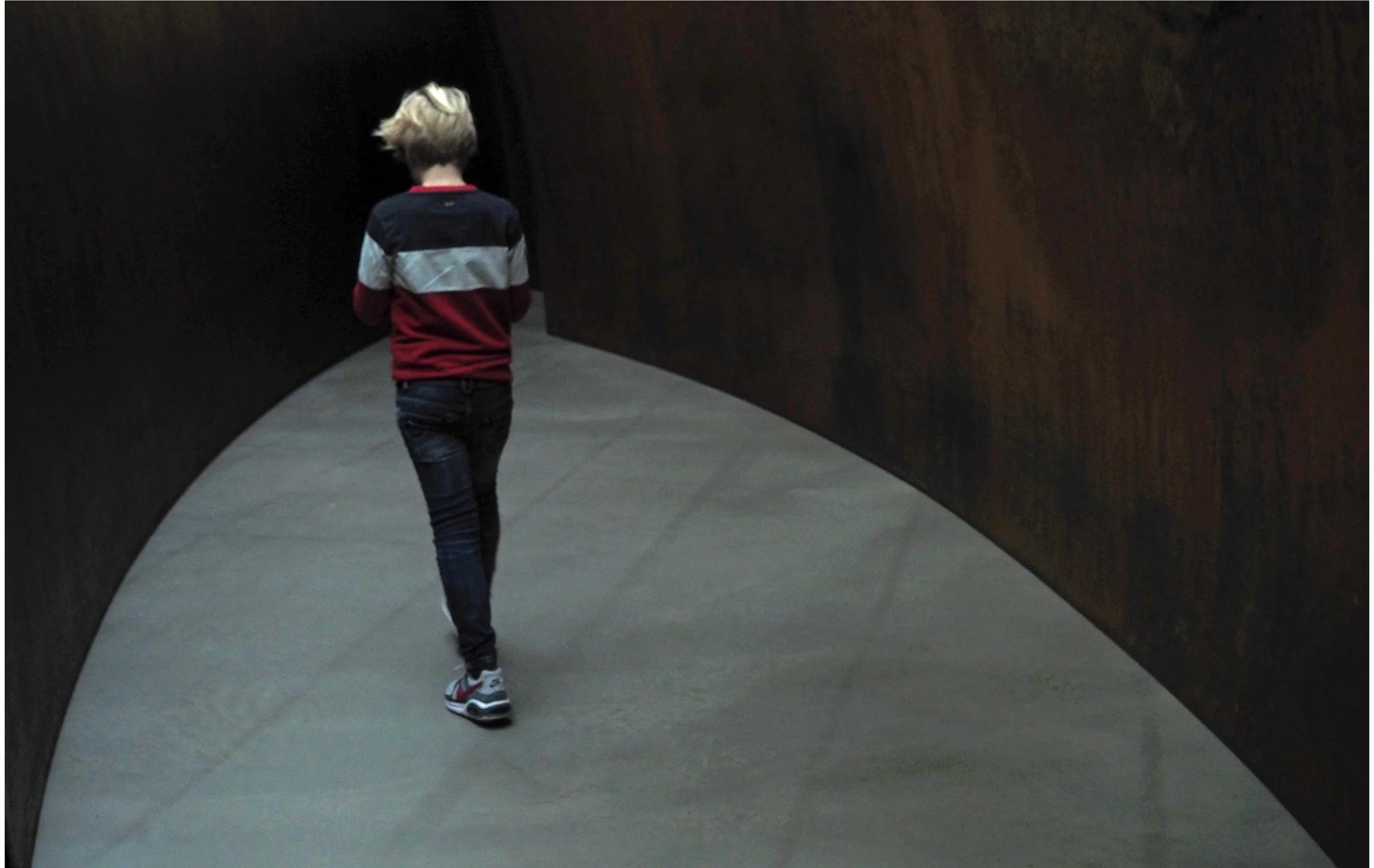 Person with blond hair walking in a dark tunnel with wooden walls.