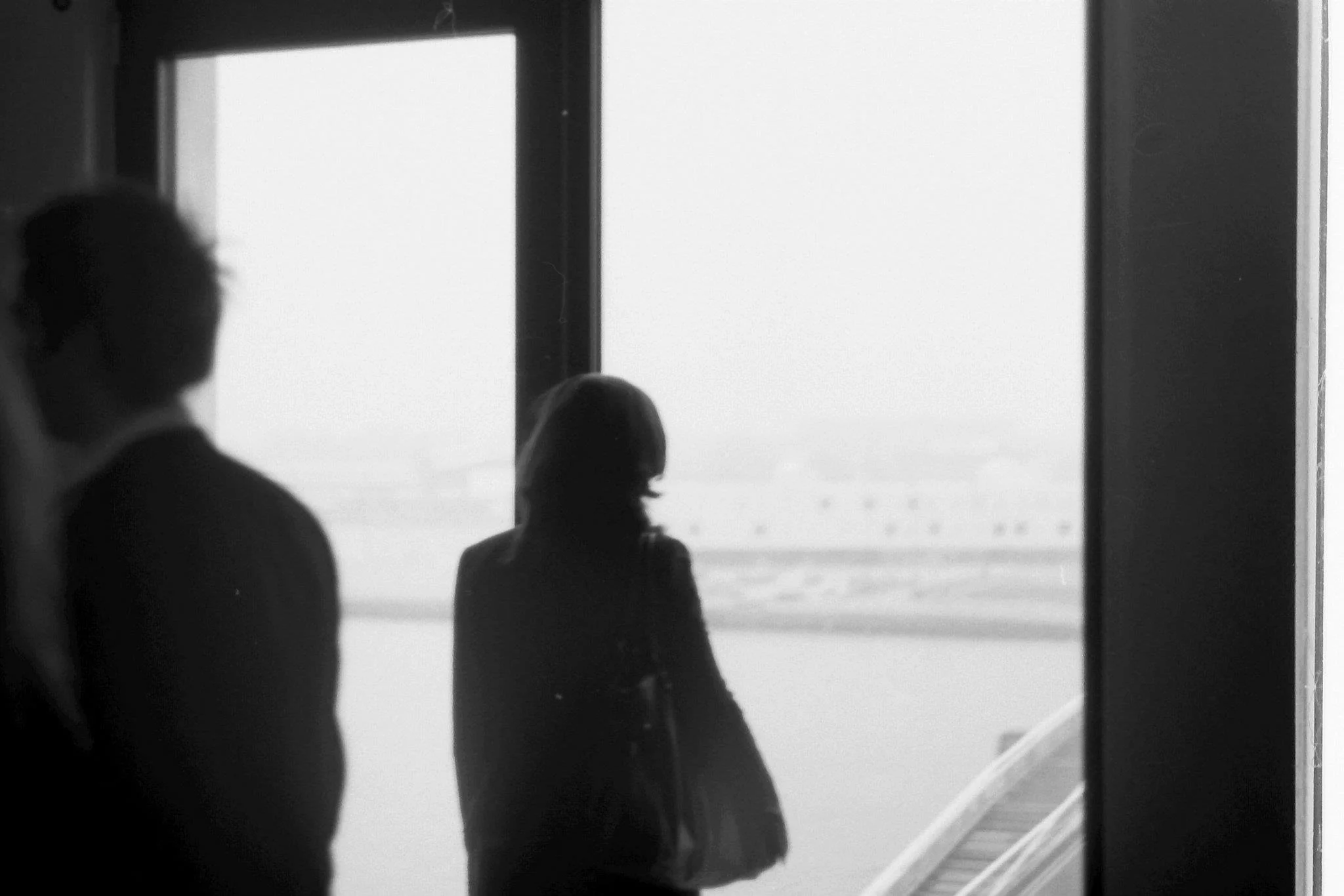 People waiting at an airport gate, seen through a large window, with a plane outside in the background.