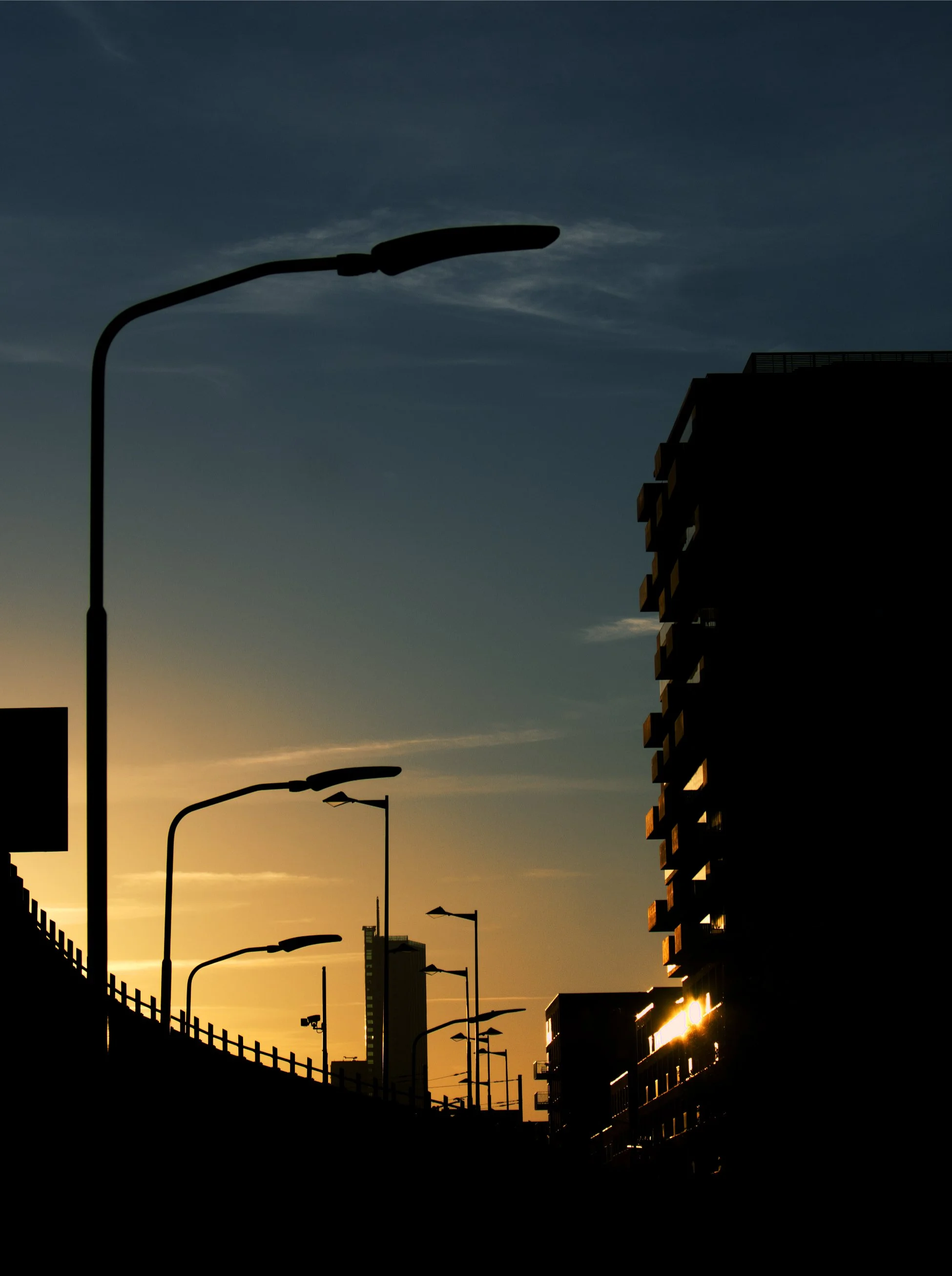 Silhouette of streetlights and buildings during sunset with a colorful sky.