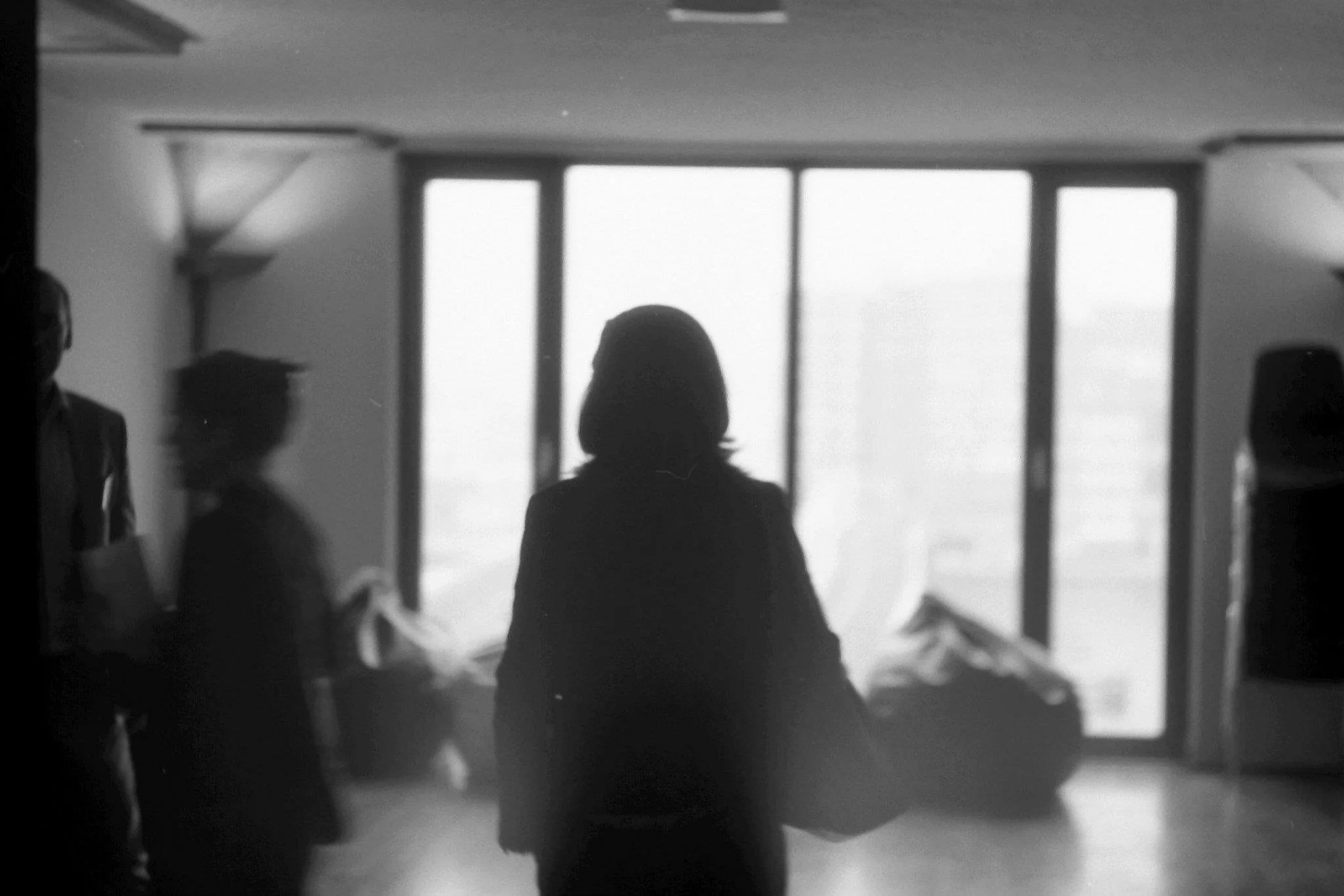 Silhouette of a woman walking inside an airport, with large windows in the background and other people in the surroundings.