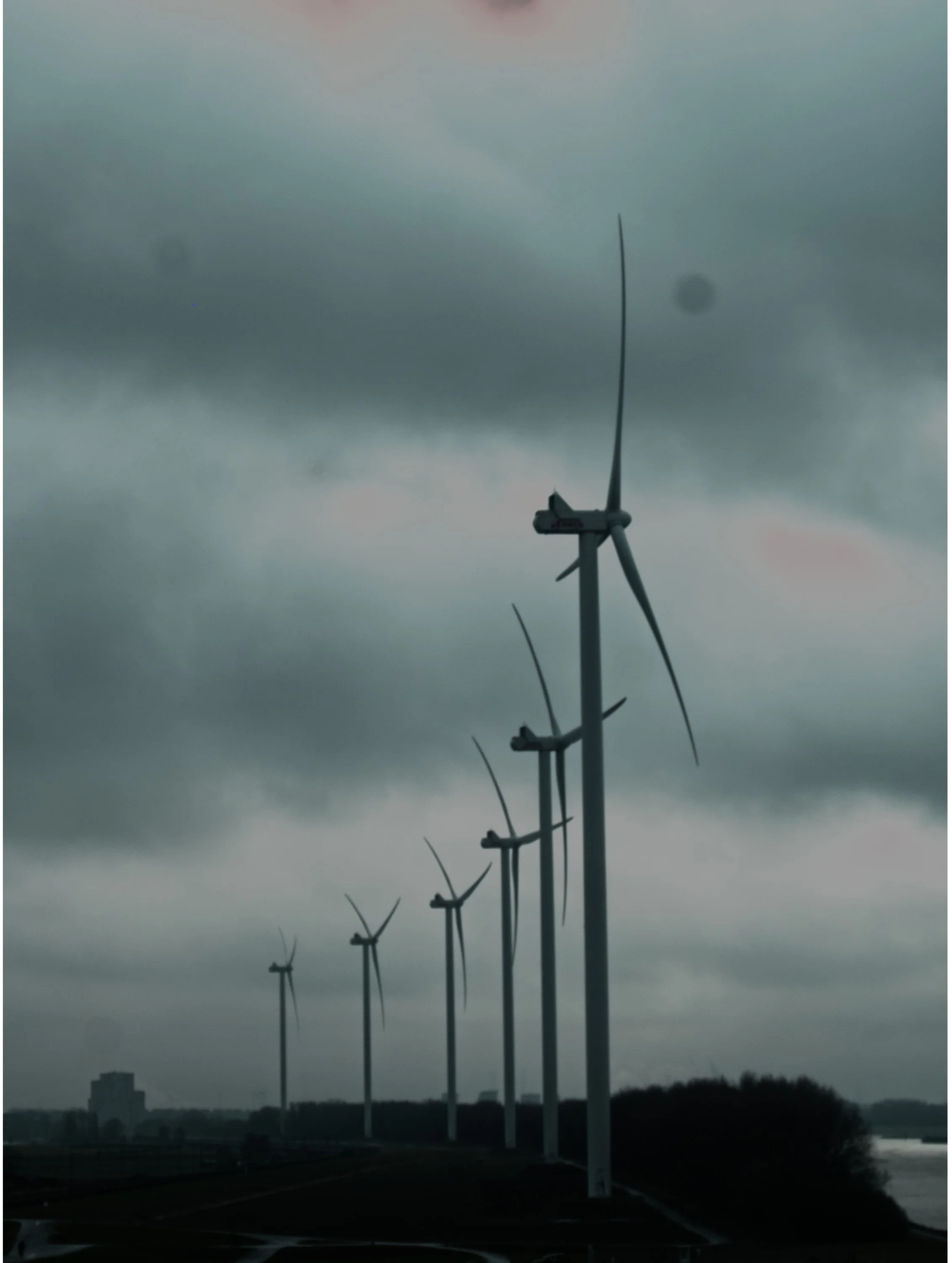 A row of wind turbines on a cloudy day along a shoreline or river.