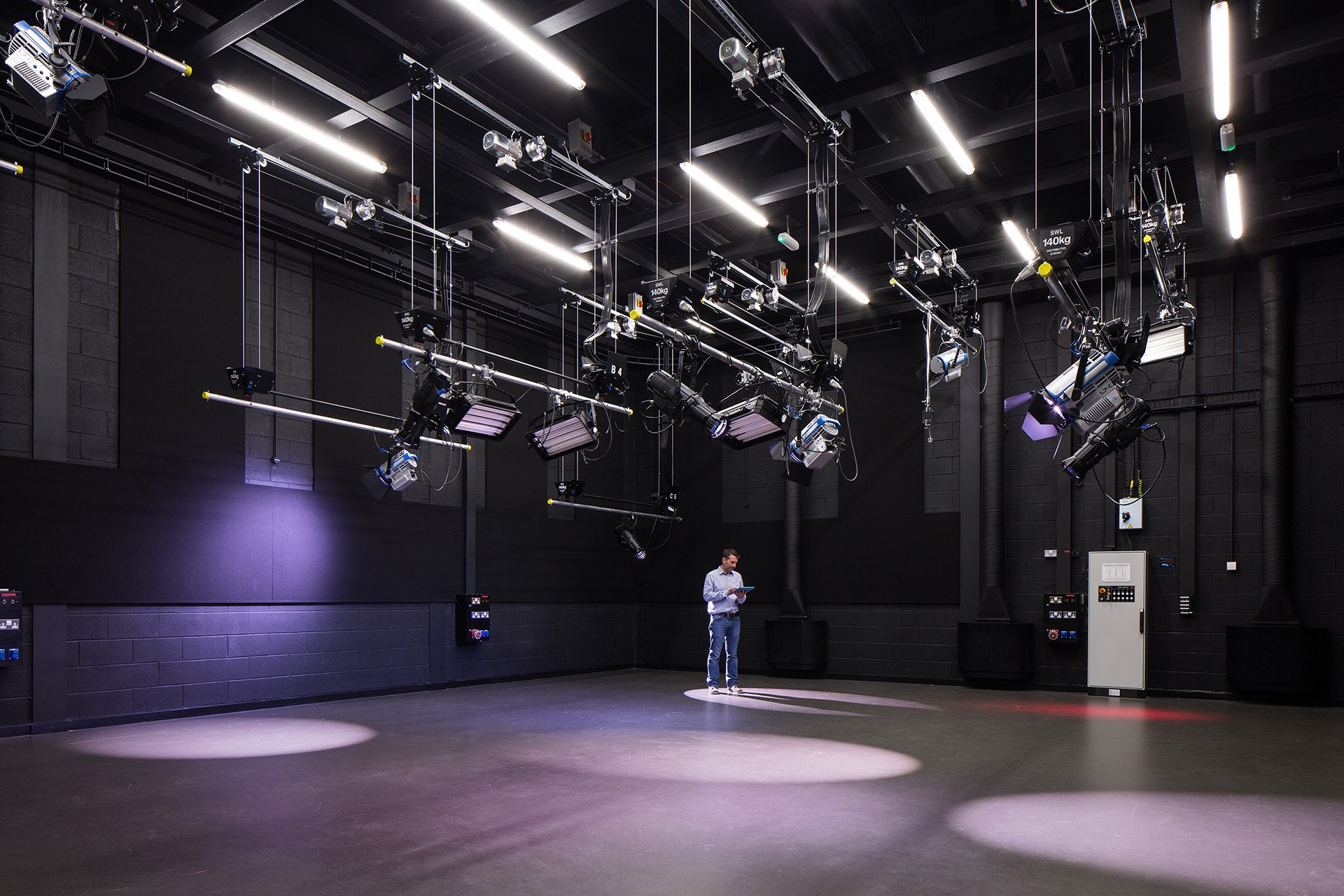 Empty black film studio with professional stage lighting, a person standing in the middle reading a book or script.