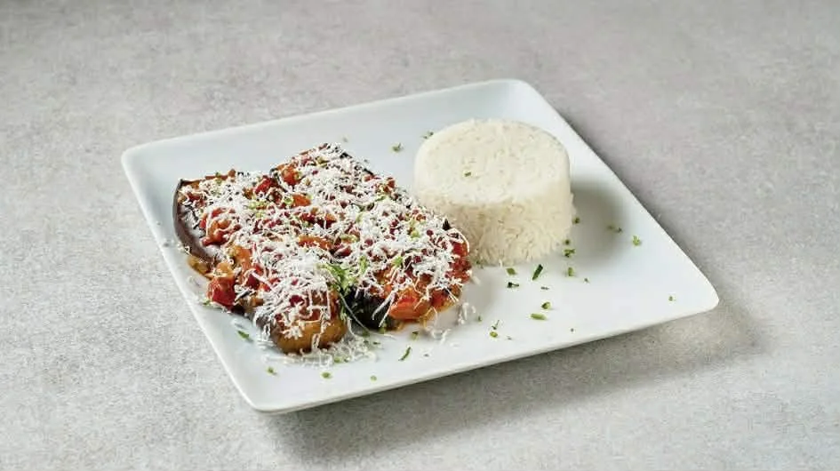 Plate of stuffed eggplant topped with cheese, served with a side of rice