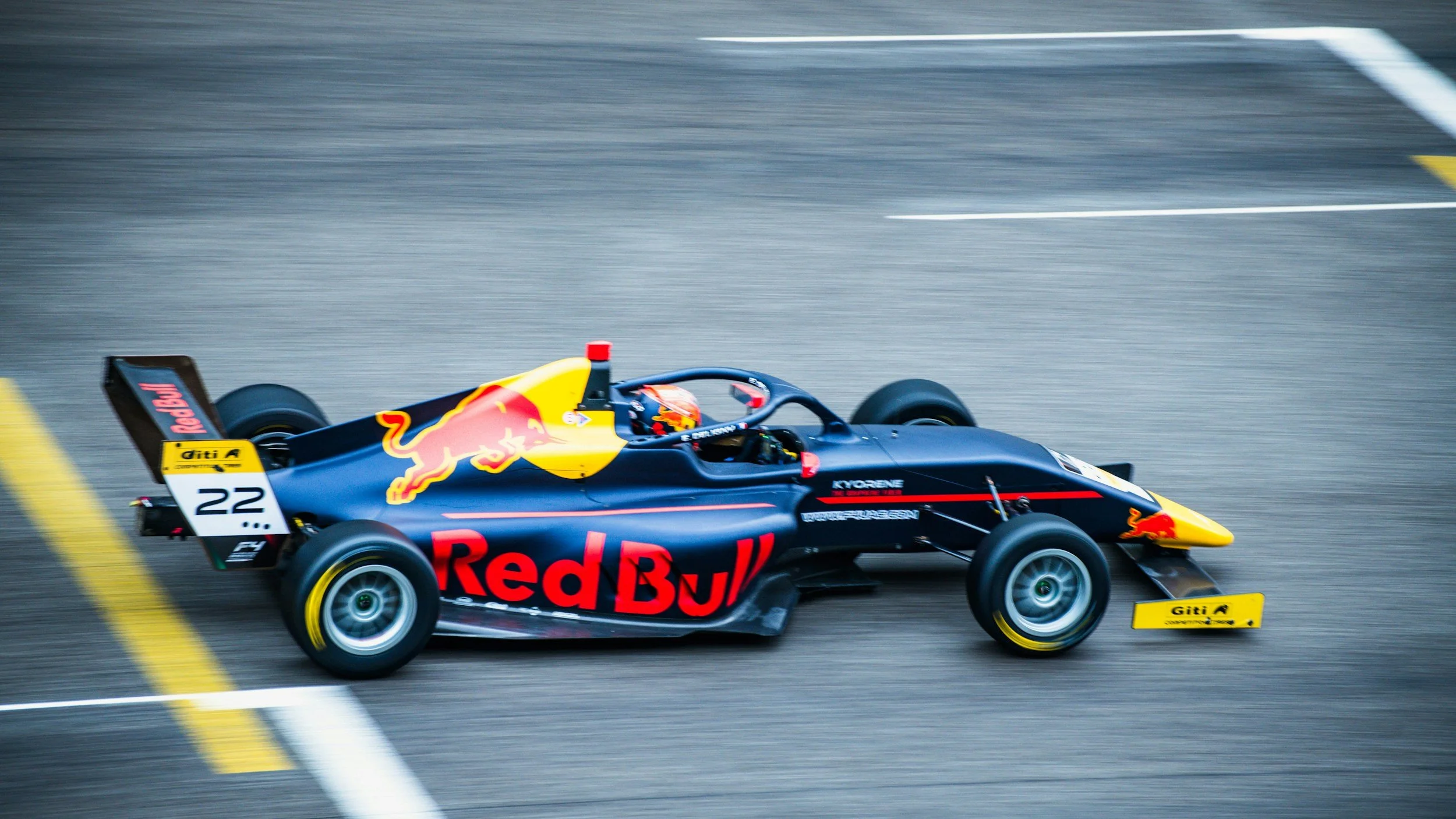 A black and yellow Formula racing car with Red Bull branding speeding on a race track.