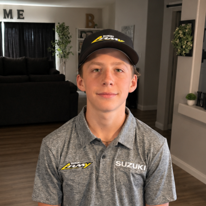 Young boy wearing a Suzuki racing cap and polo shirt, standing indoors in a living room.