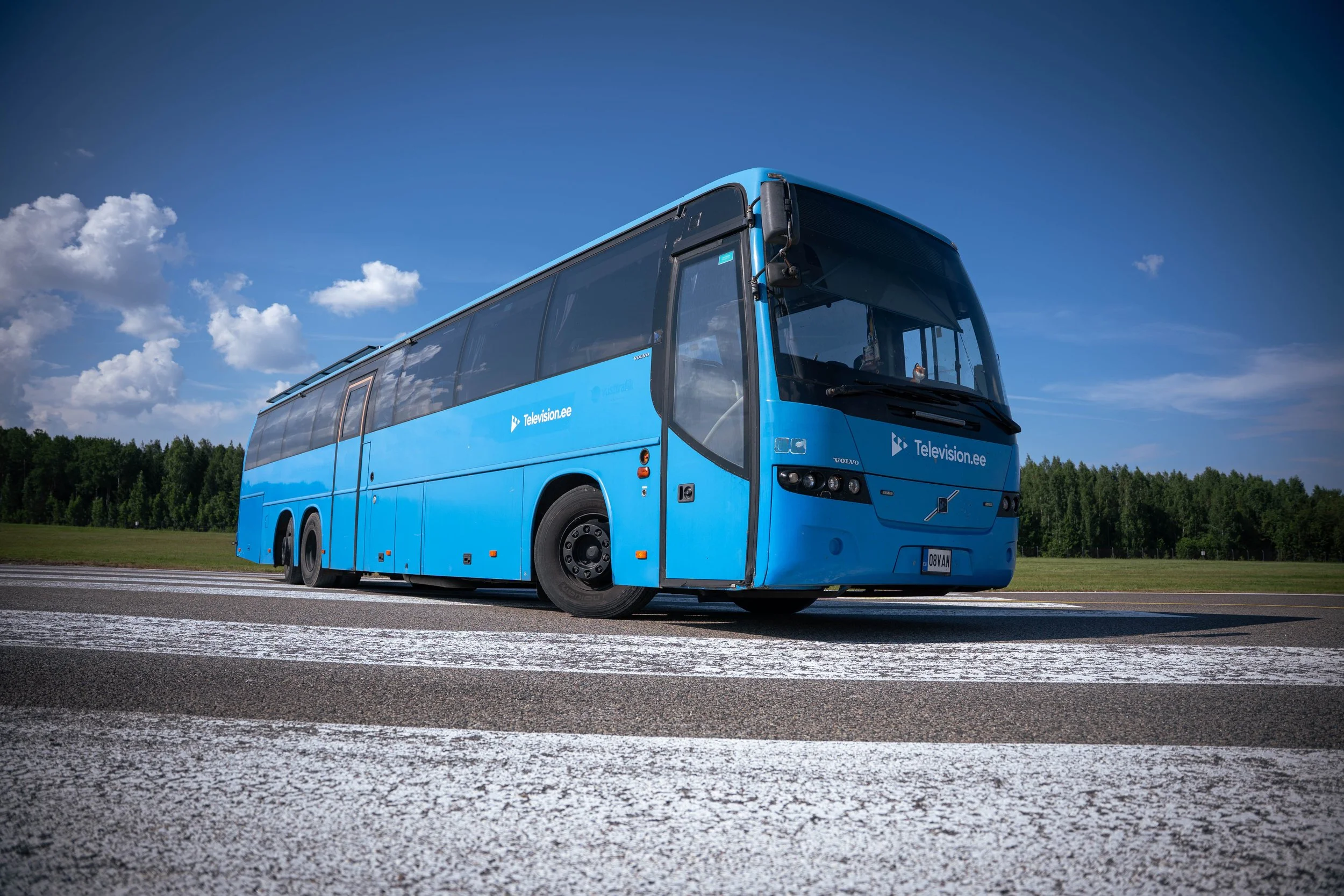 Blue bus with 'Television.ee' logo on an empty road under a partly cloudy sky.