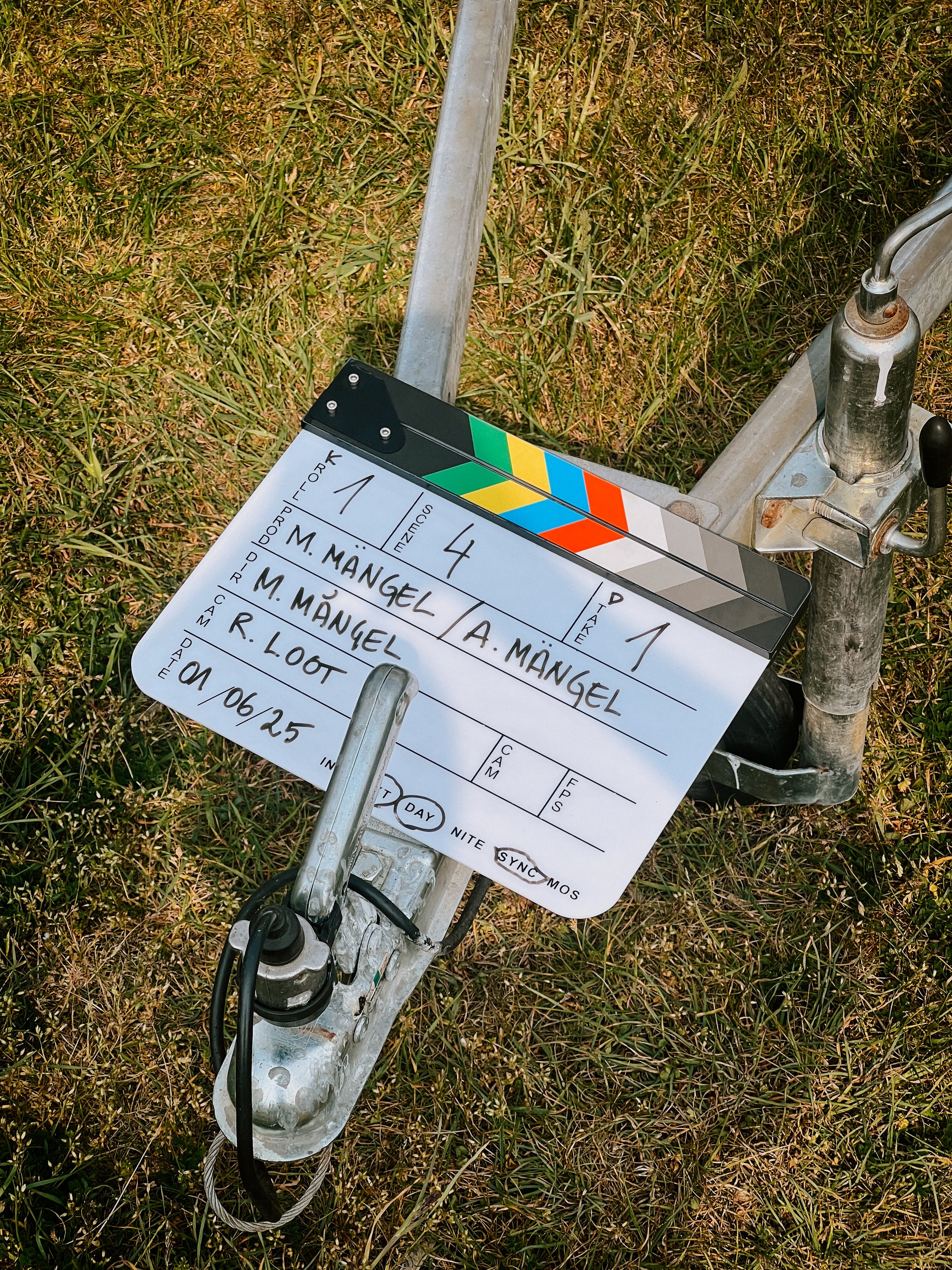 A film clapperboard on a grassy field. The clapperboard displays information about a scene, shot, director, and date.