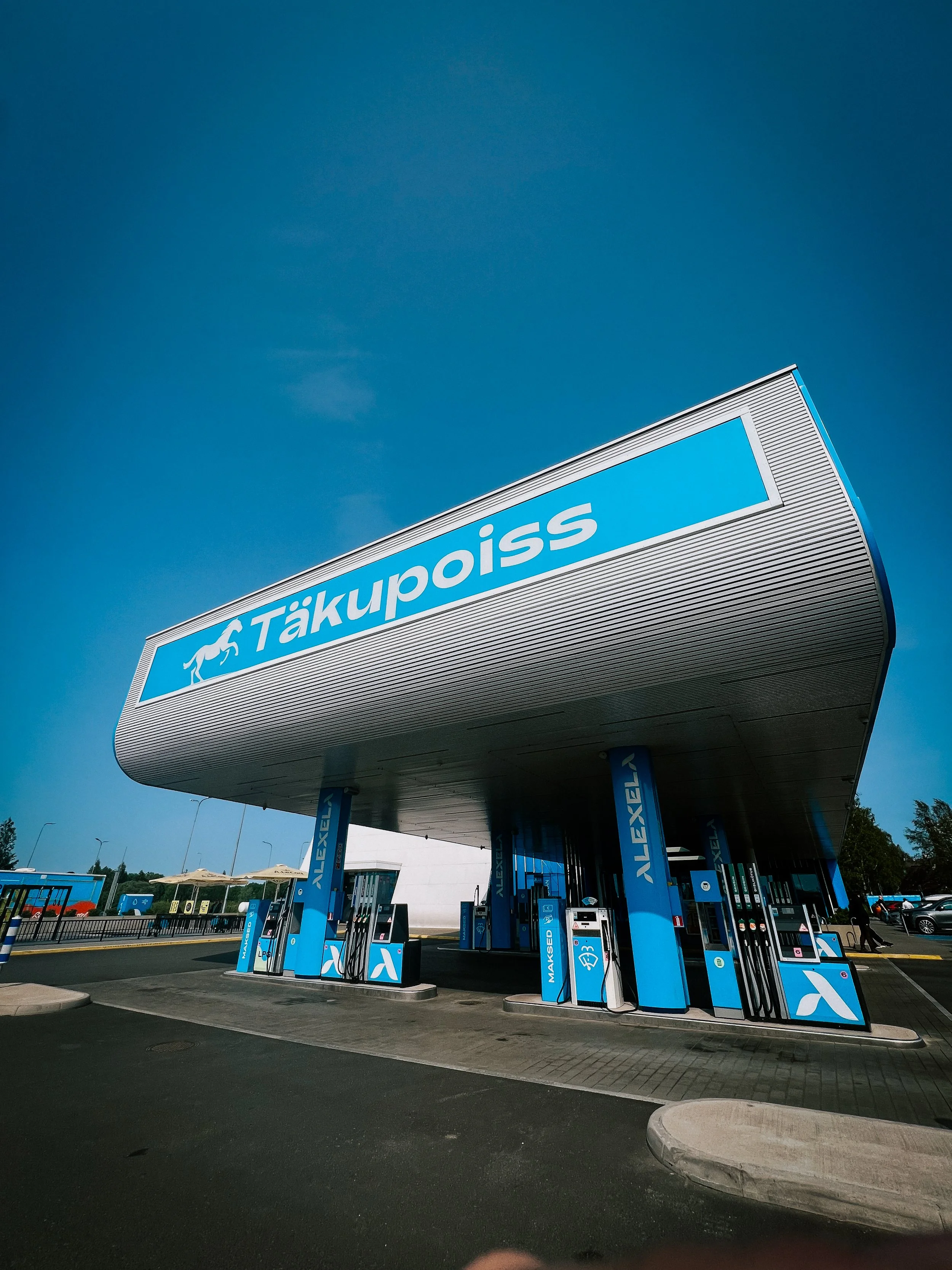 Täkupoiss gas station with blue branding, fuel pumps, and a canopy under a clear blue sky.
