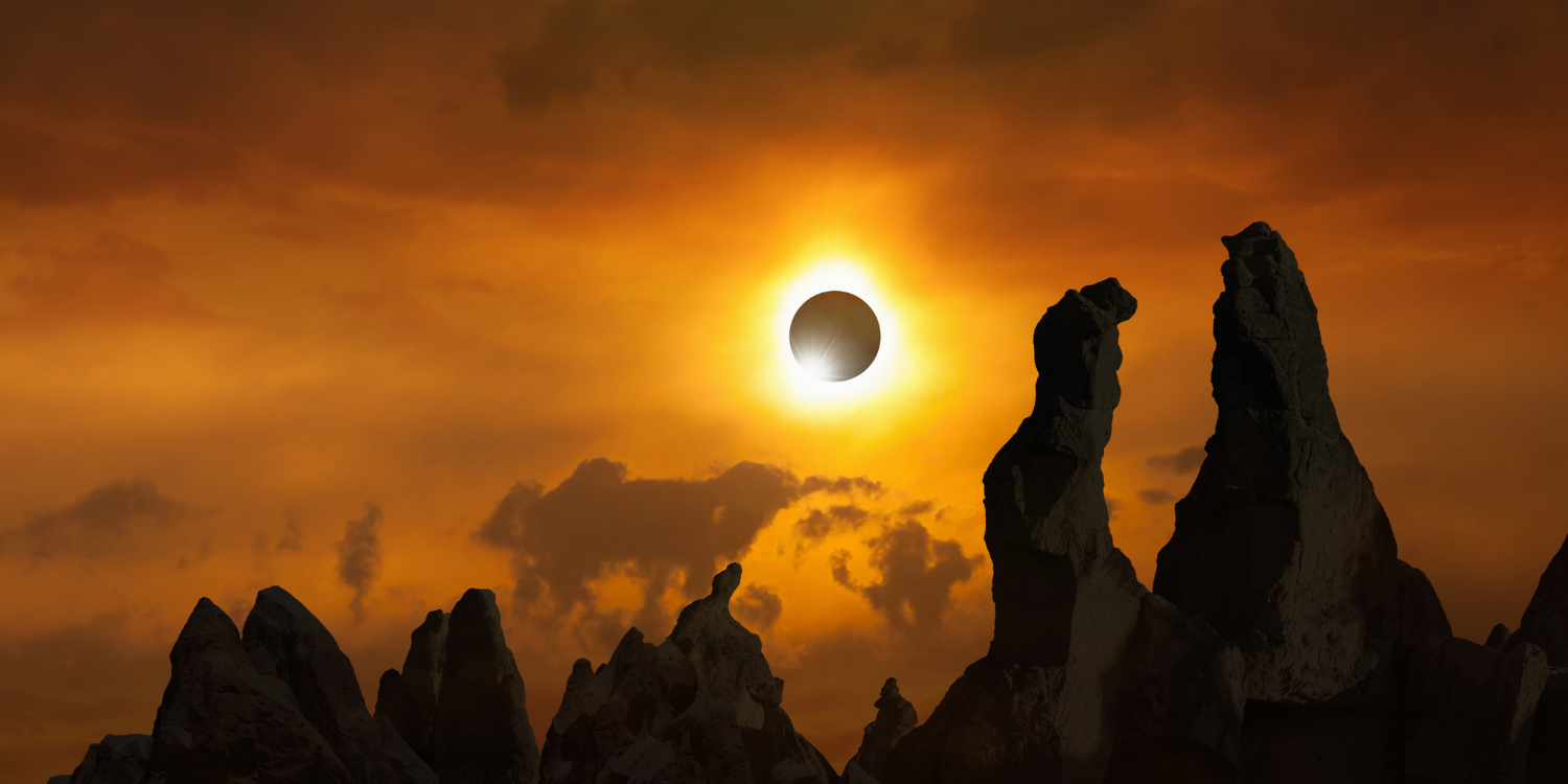 Orange sky displaying a partial eclipse over a rocky terrain
