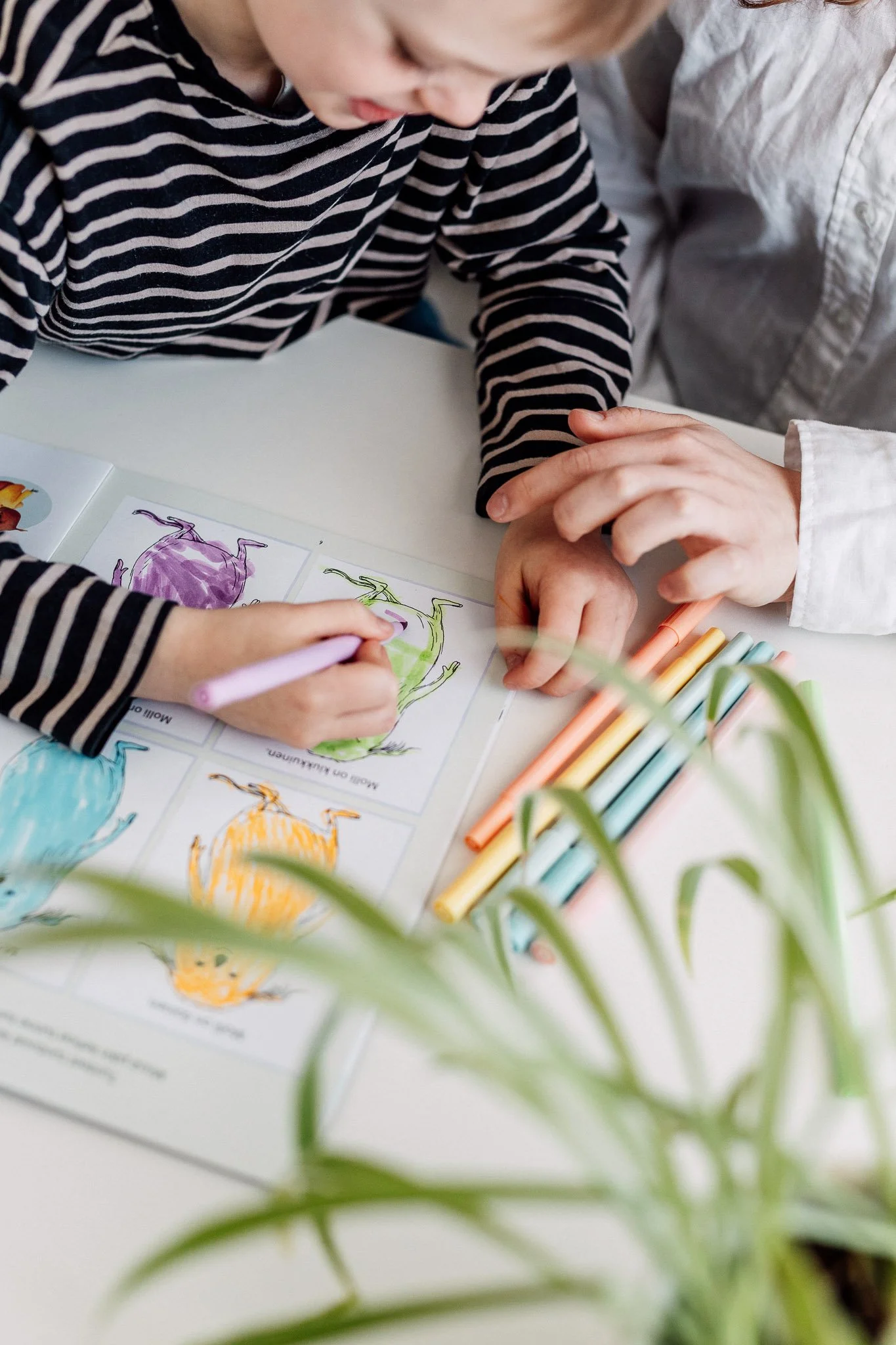 Puheterapeutti ja kuusivuotias asiakas harjoittelevat tunnetaitoja sekä värejä. Lapsi värittää kirjaa.
