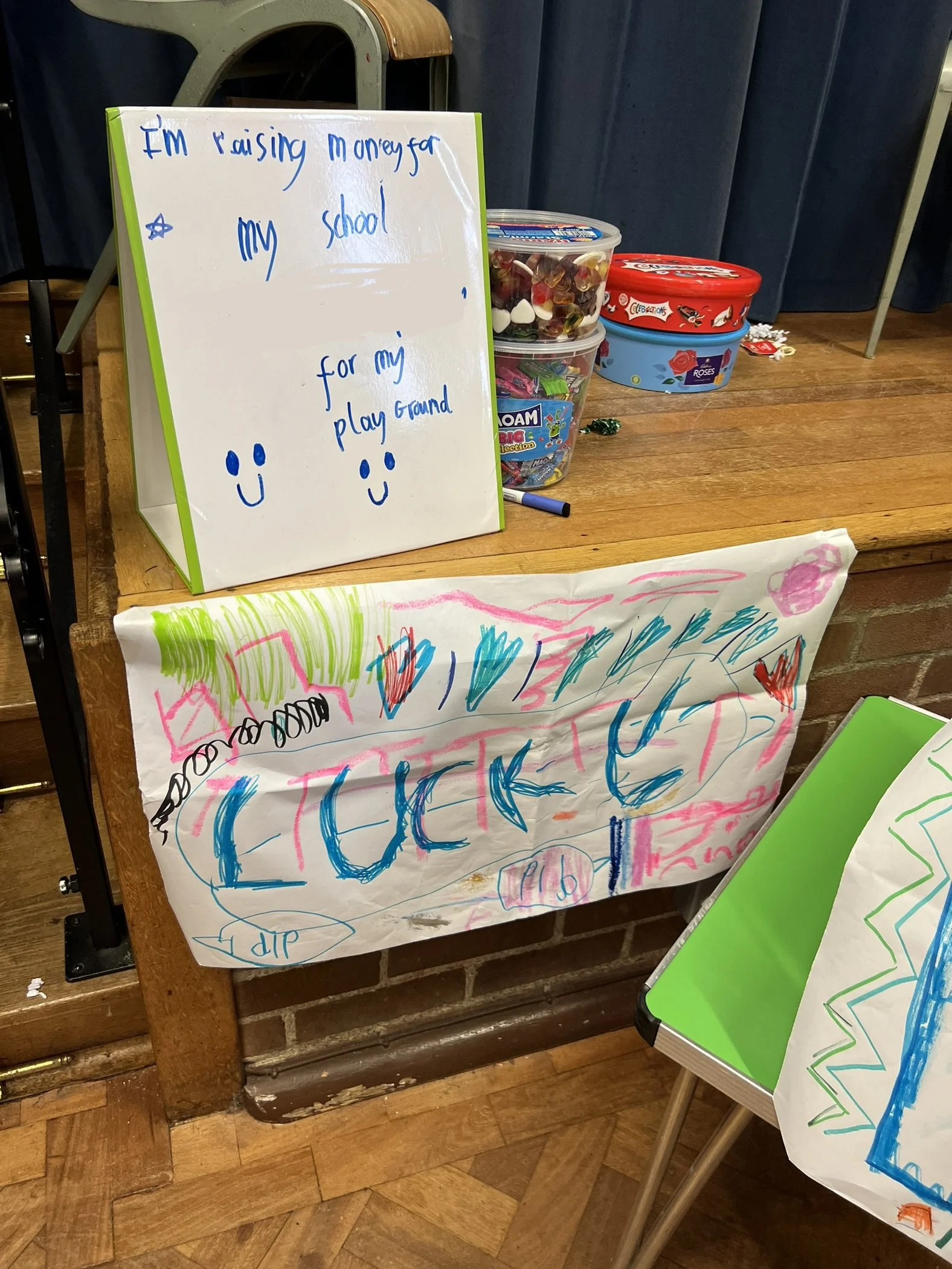 Handmade sign and drawings on paper promoting a chicken-themed event. The sign reads 'I'm raising money for my school for my play ground' with smiley faces. The paper features colorful scribbles and the word 'CHICKEN' in large letters.
