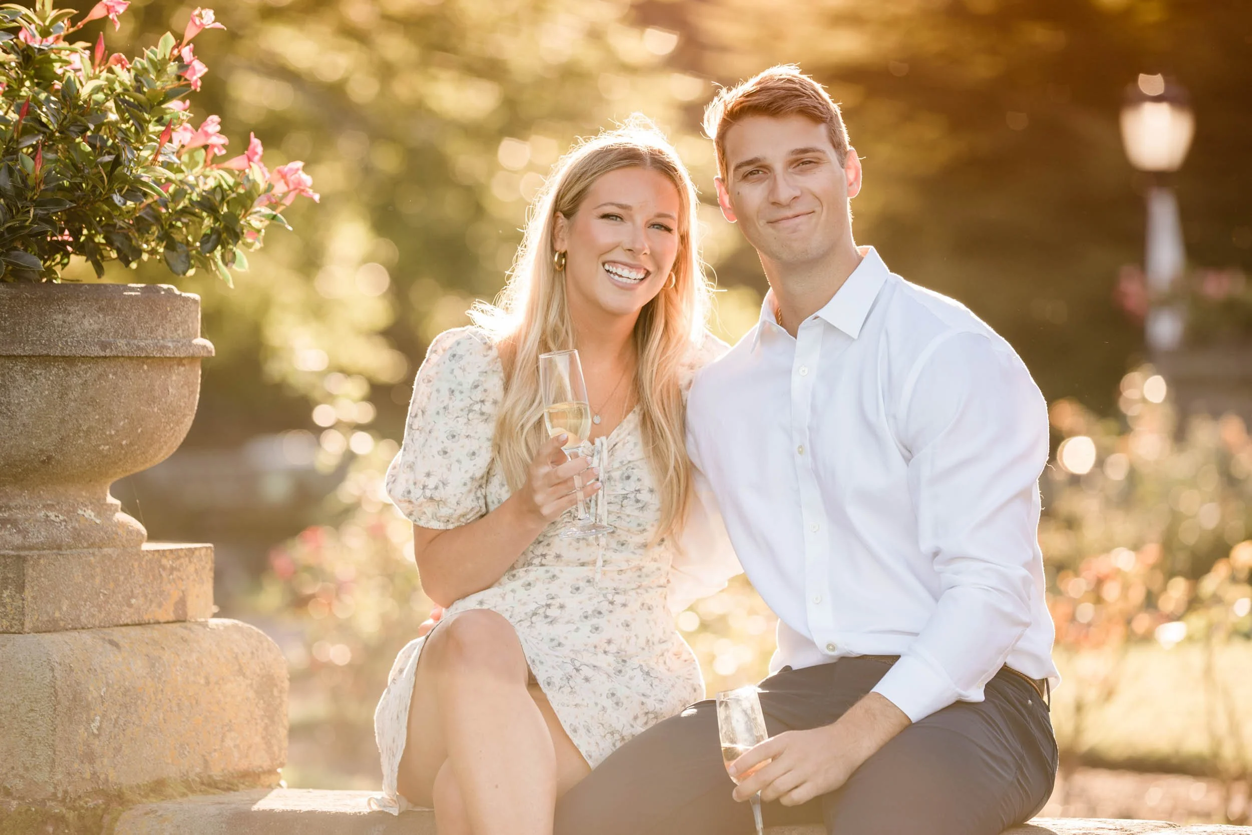 A couple laughing with champagne in a Newport rose garden at golden hour