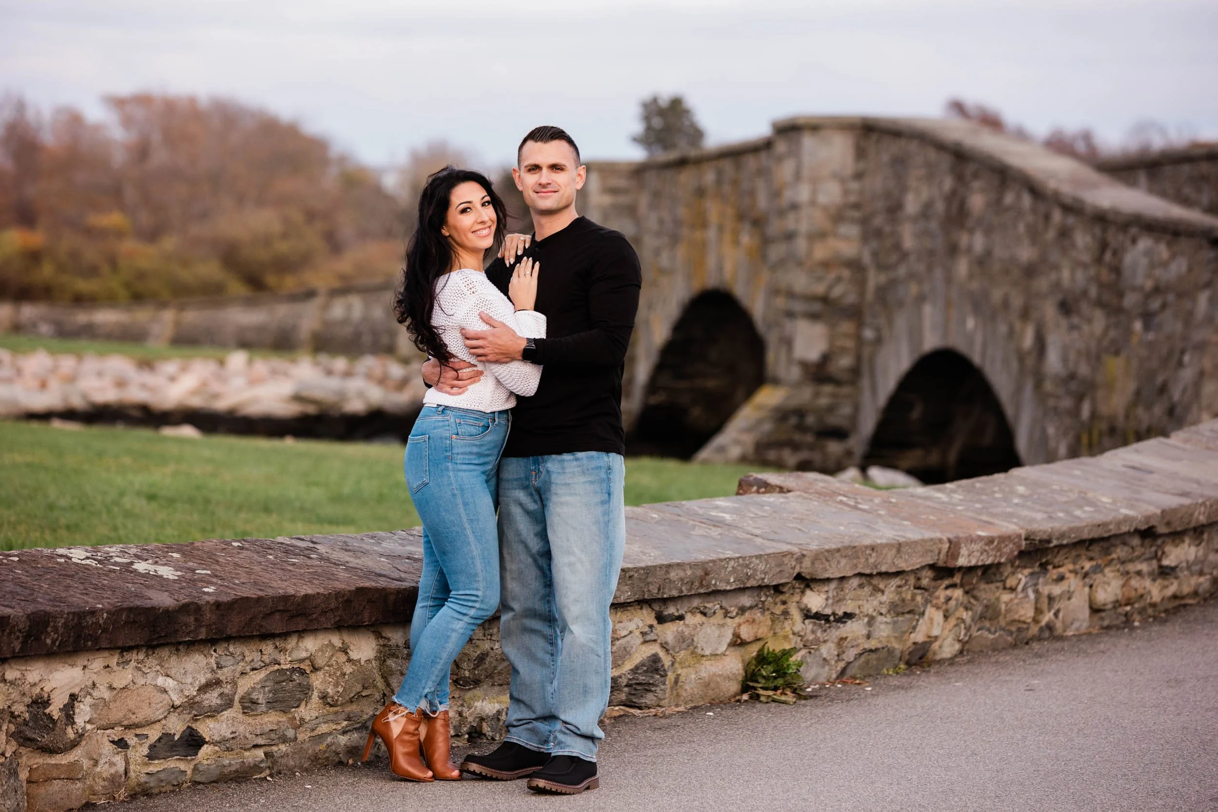 An engaged couple at a stone arch bridge on Ocean Drive in the fall