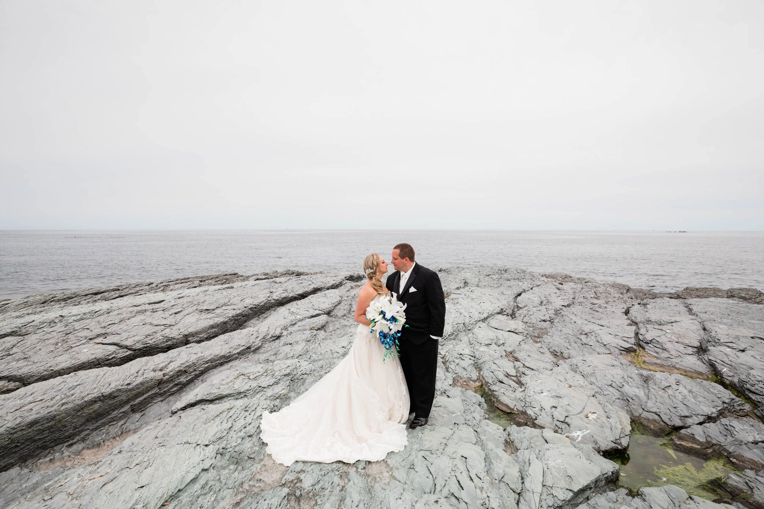 A bride and groom kissing on the rock ledges along the water at OceanCliff