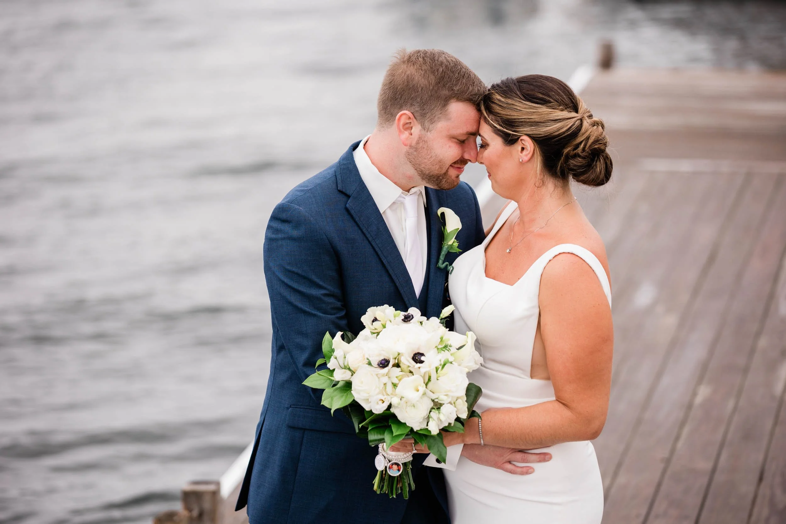 A bride and groom forehead to forehead on the dock at Regatta Place in Newport