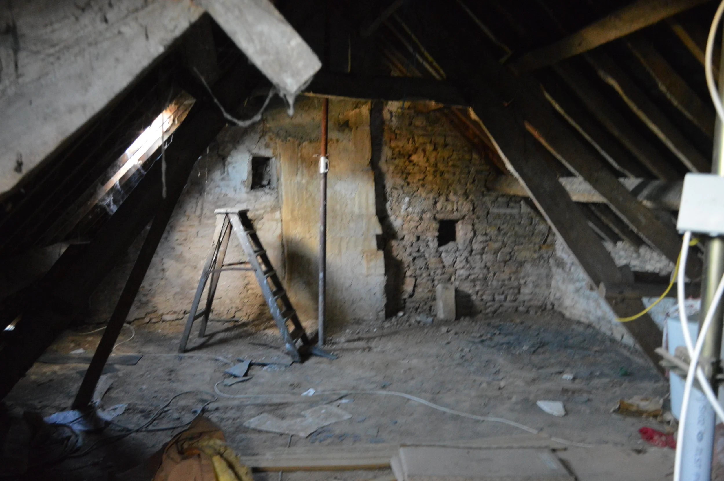 Attic space with exposed roof beams, a ladder, and construction debris, indicating renovation or construction work.