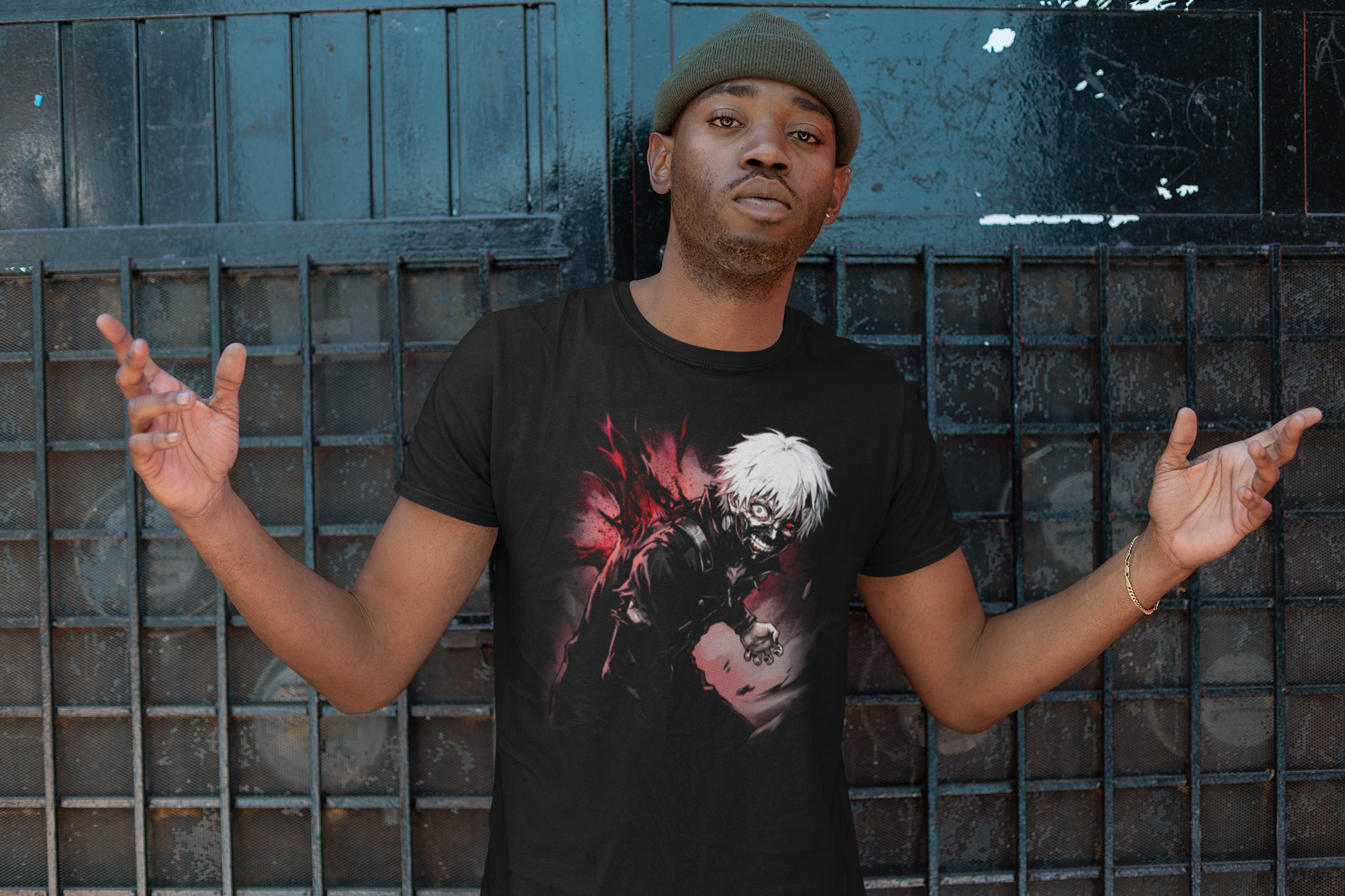 A young man with a neutral expression wearing a green beanie and a black graphic t-shirt poses with his arms raised, standing against a dark metal fence.
