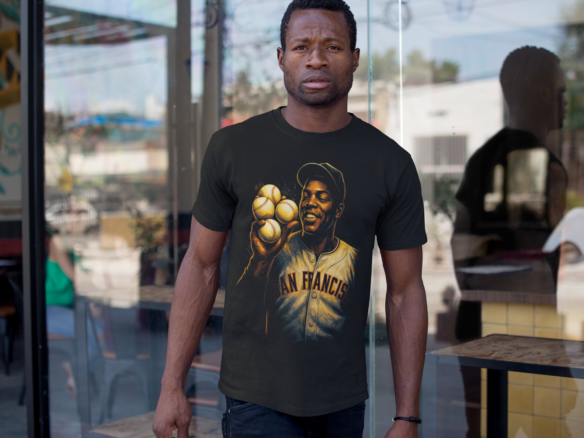 A man wearing a black T-shirt with a graphic of a baseball player holding six baseballs and the words 'San Francisco' printed on the front, standing in front of a glass window.
