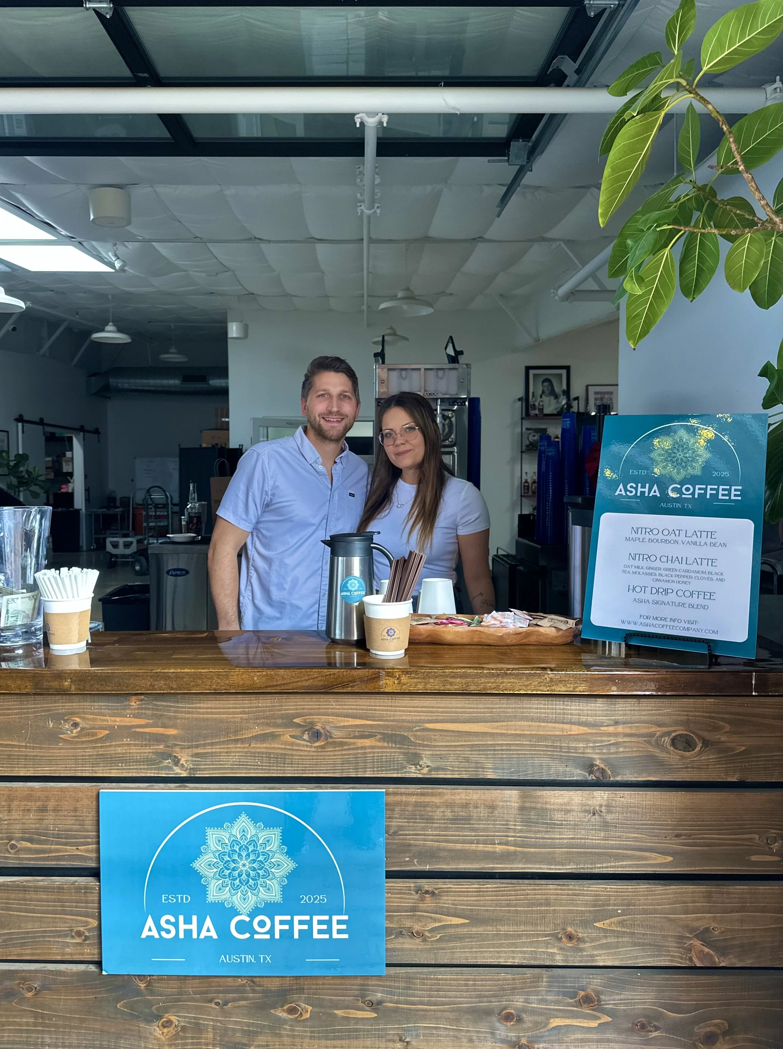 Two people behind a wooden coffee counter at Asha Coffee in Austin, TX, with a menu sign displaying various coffee drinks.