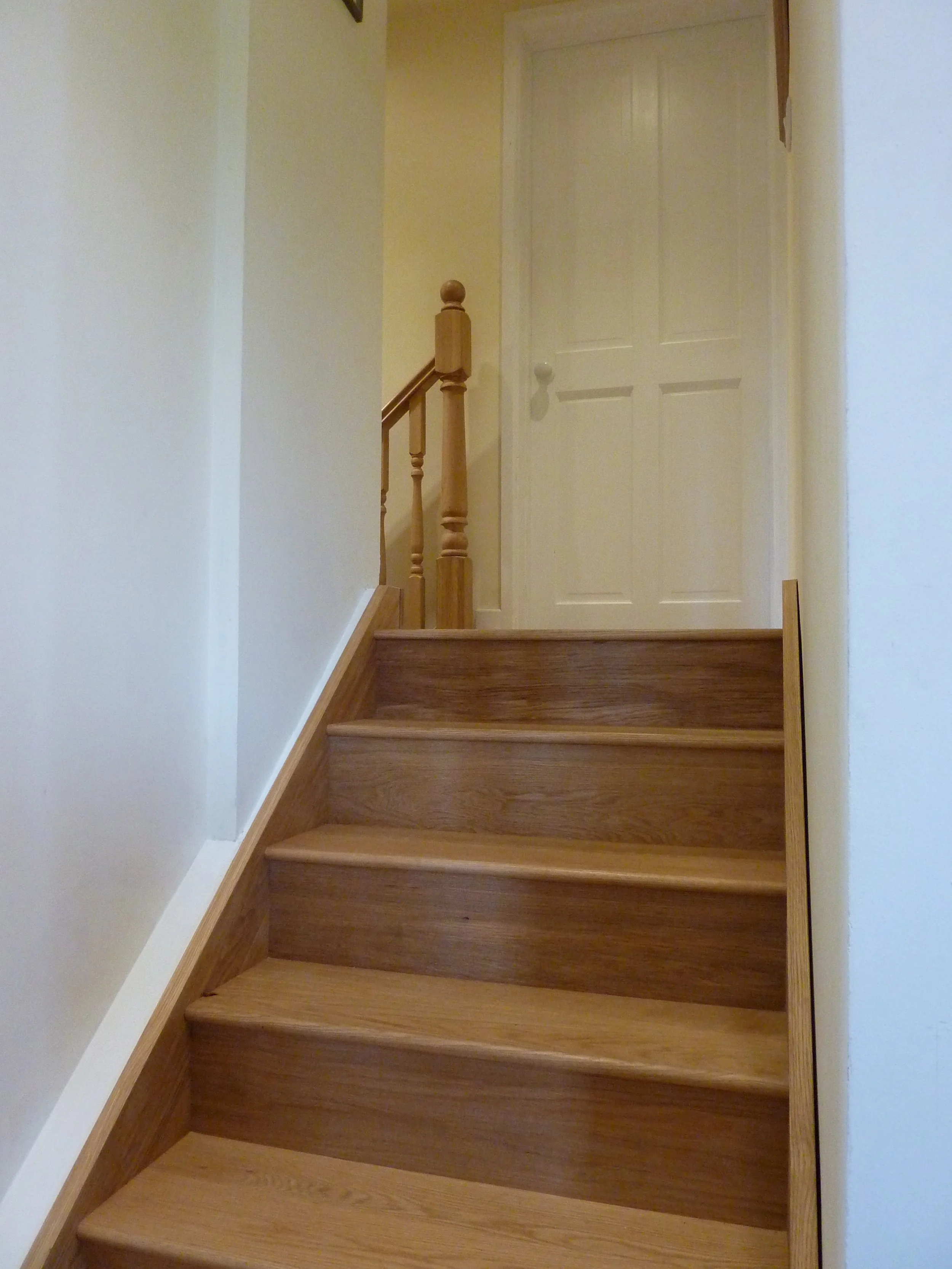 Wooden staircase leading to a closed white door in a house interior.