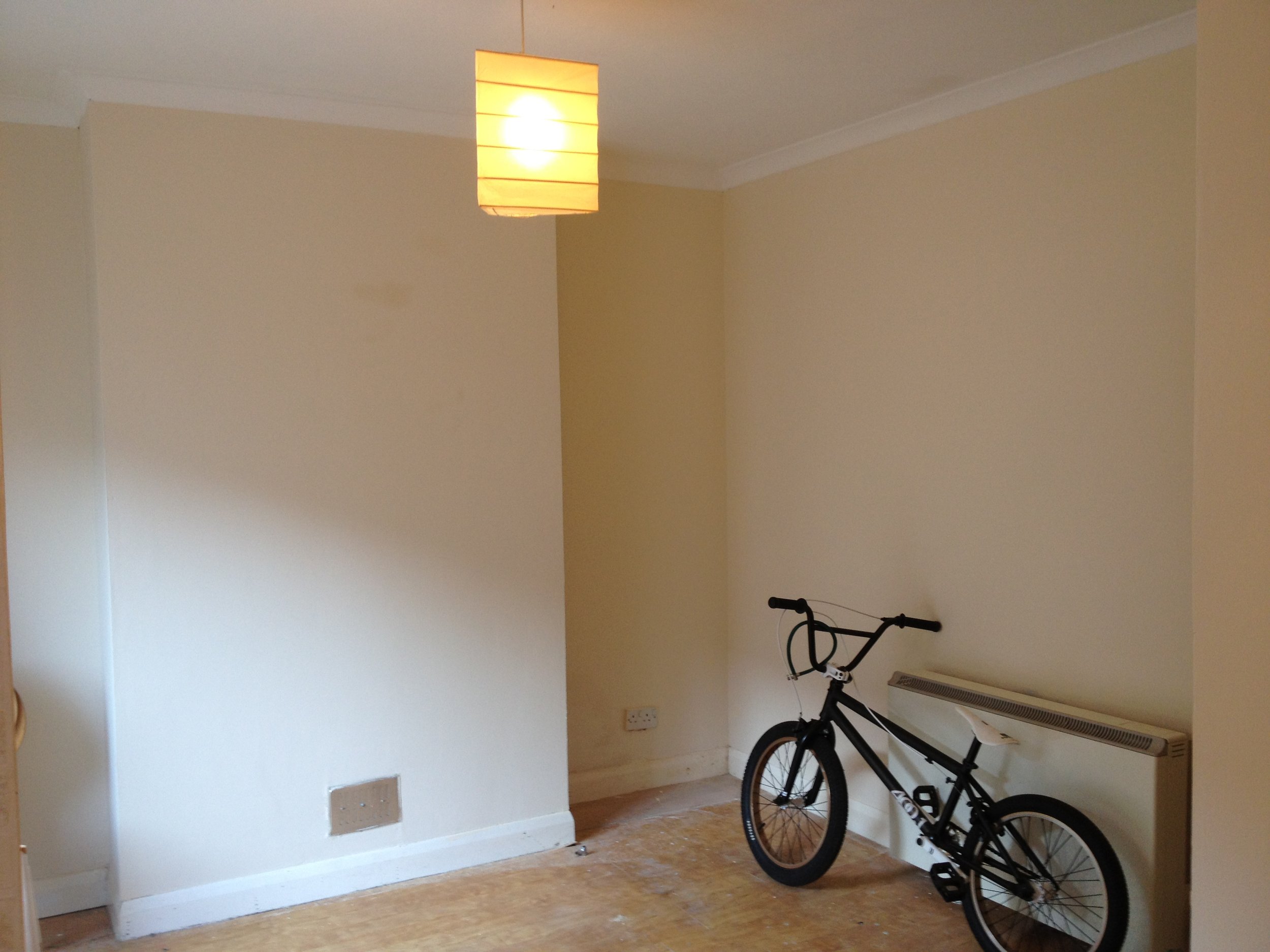 Empty room with a yellow wall, a bicycle, and a heating radiator.