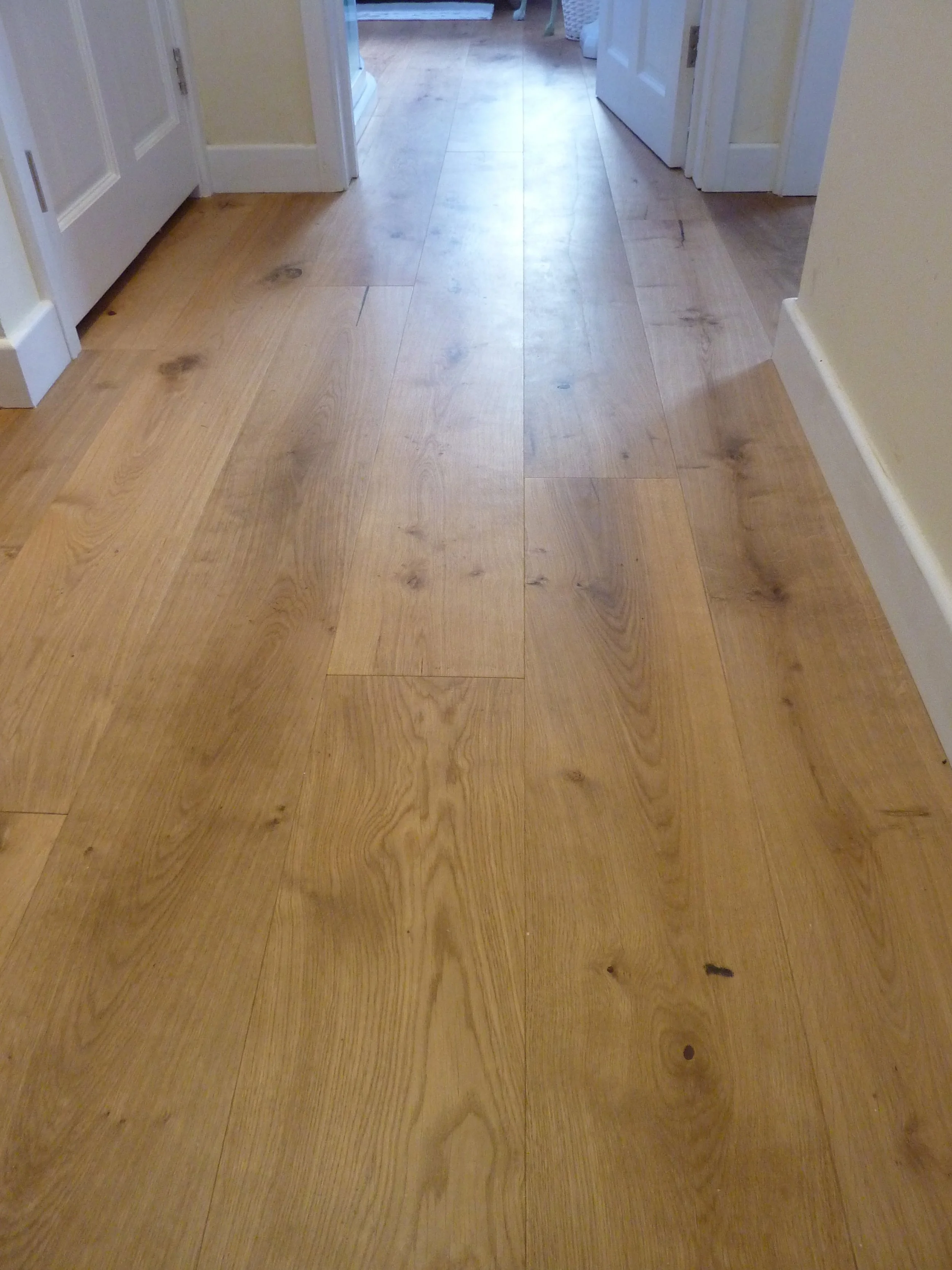 Wooden floor in a hallway with doors on either side leading to other rooms.