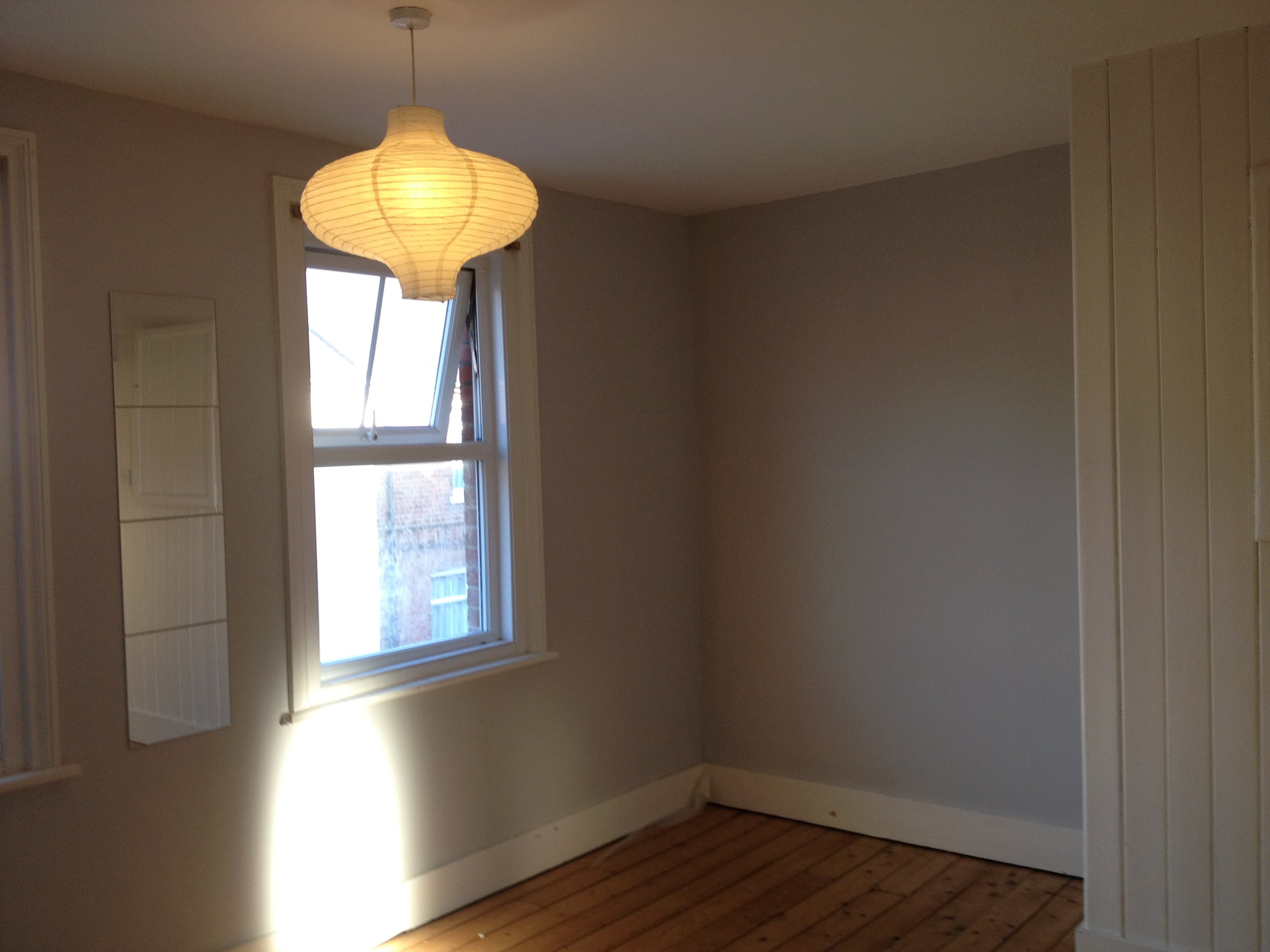 A room with a window, a hanging light fixture, and wooden flooring.