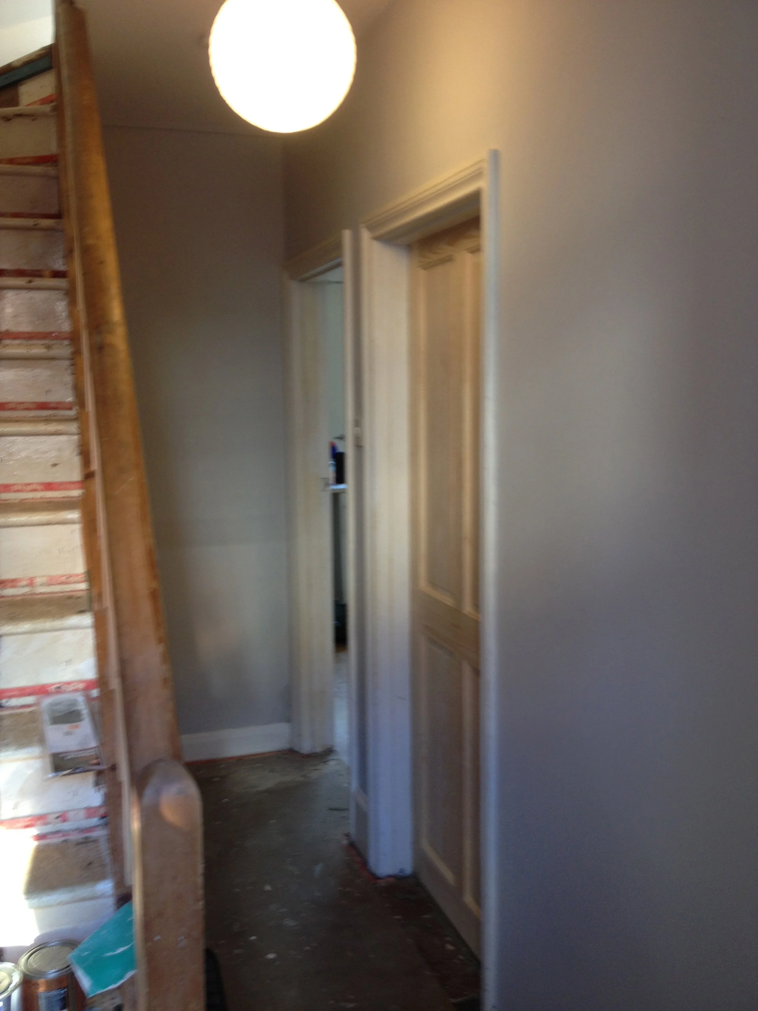Interior view of a hallway under renovation with unfinished walls, a door frame, and construction supplies on a wooden shelf.