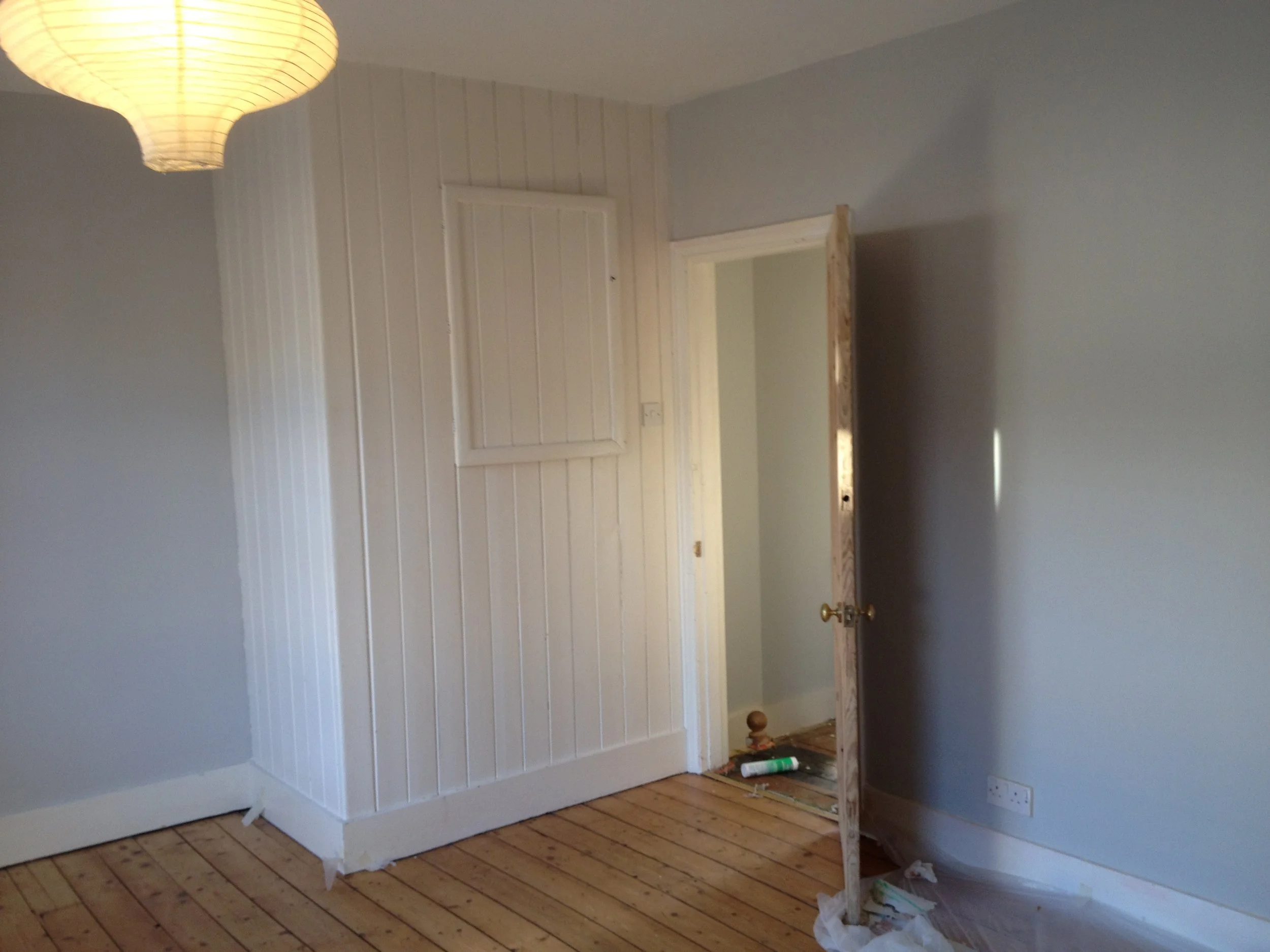 Interior of a room under renovation with a partially built white wooden structure, trash on the floor, and a ceiling light fixture.
