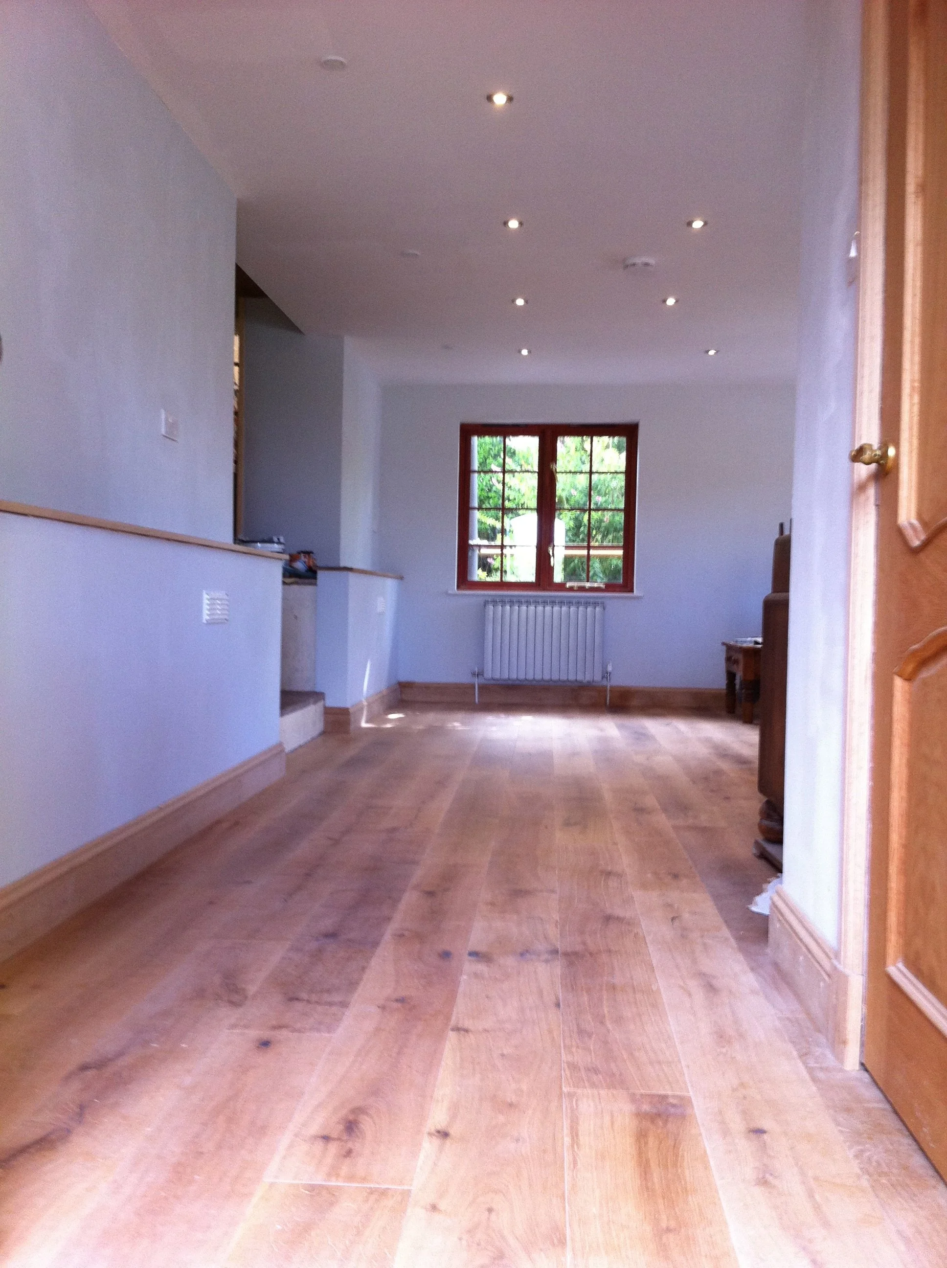 Empty living room with hardwood flooring fitted, a large window, and a radiator beneath the window.