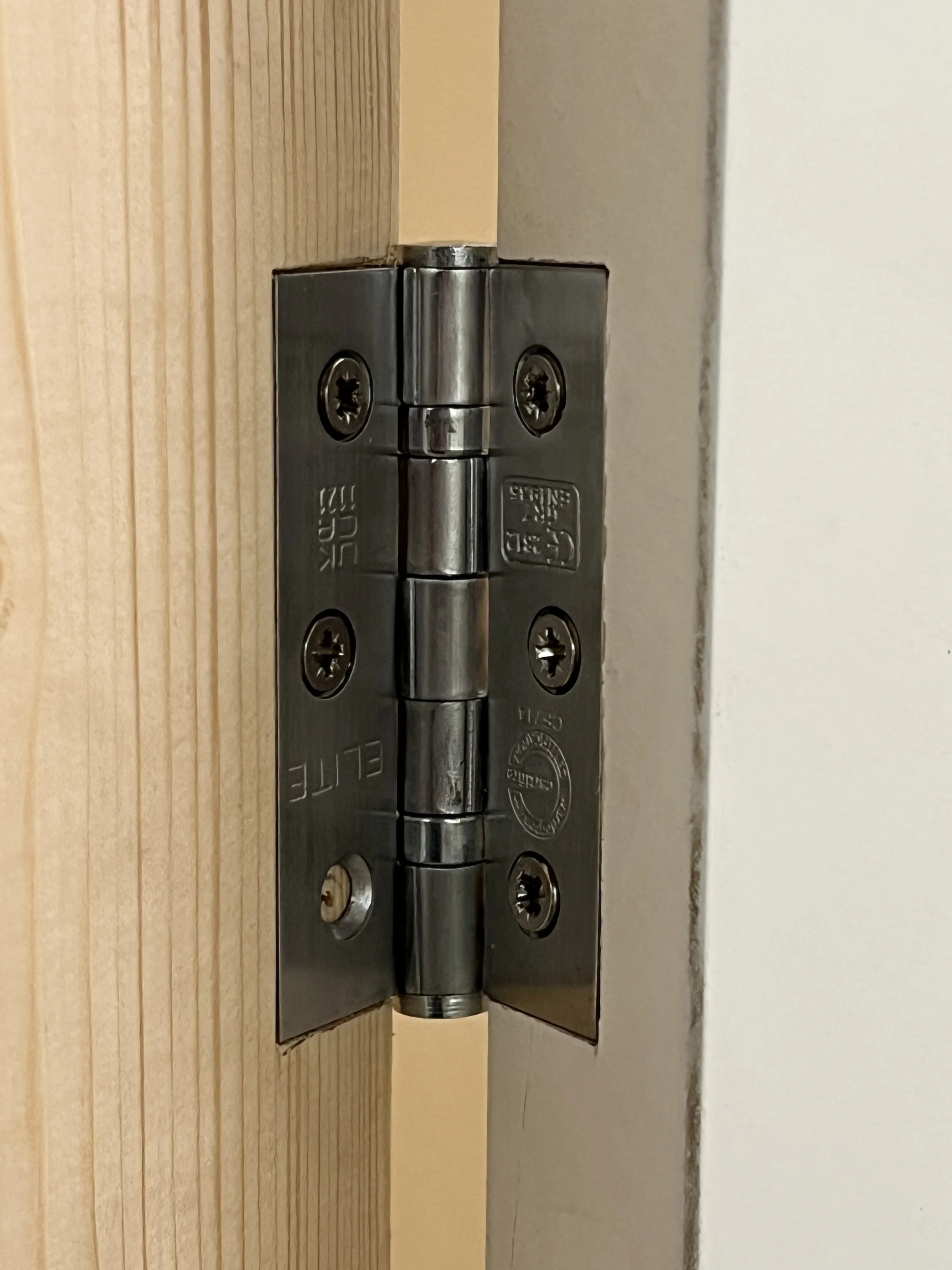 A metal hinges partially embedded in unfinished wood door and painted drywall wall.
