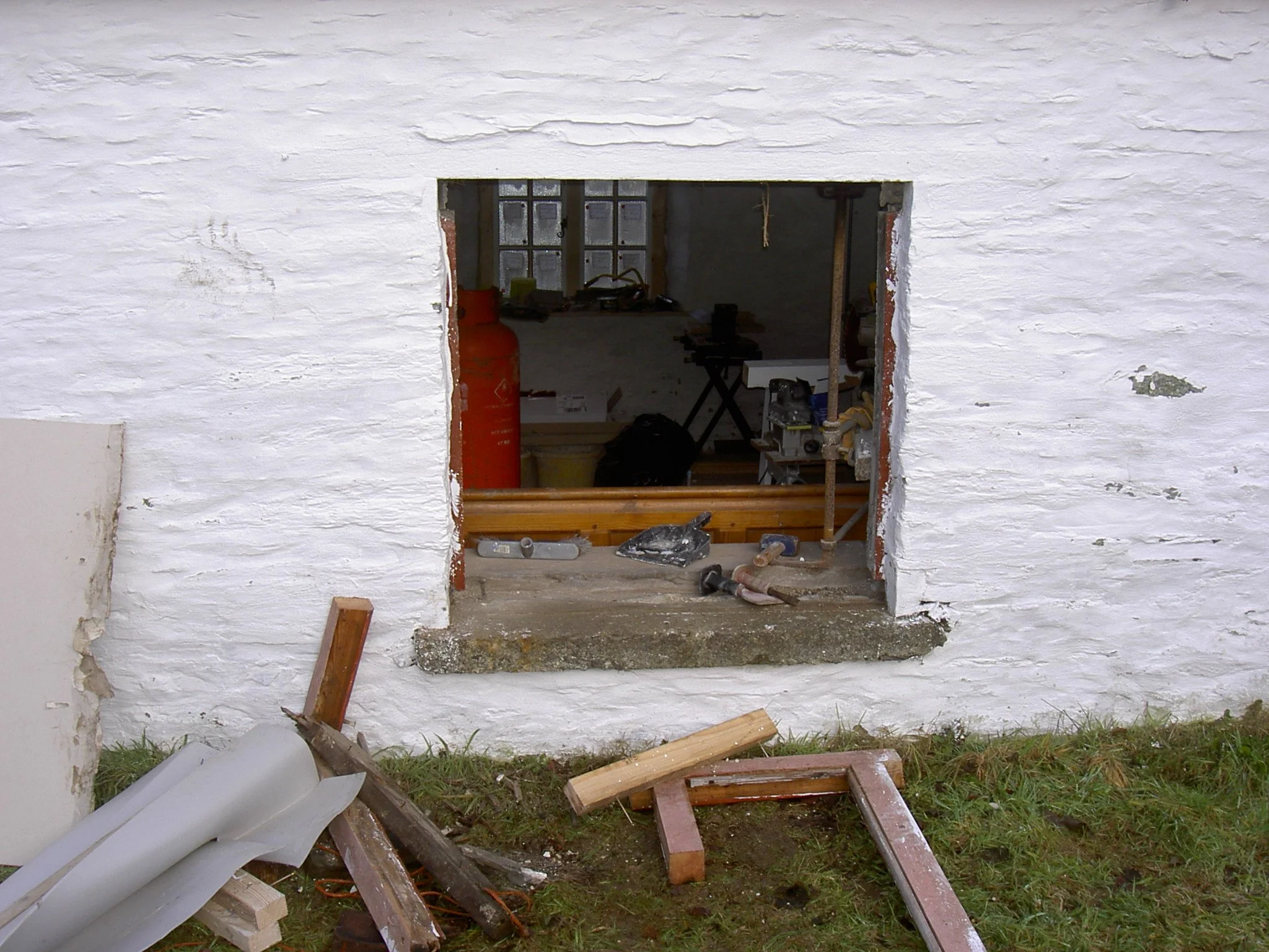 A house wall with a large opening under construction, showing construction tools and materials inside and outside on the ground.