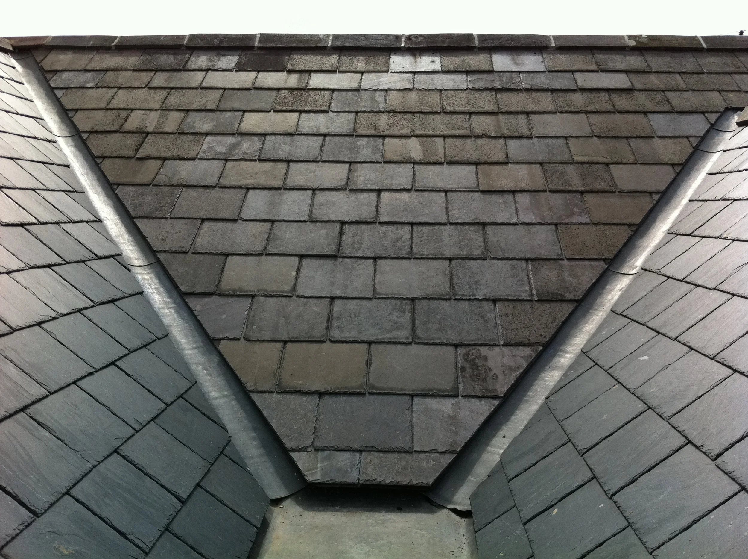 Close-up of a roof with overlapping welsh blue slates, a lead valley and rubber gutter.