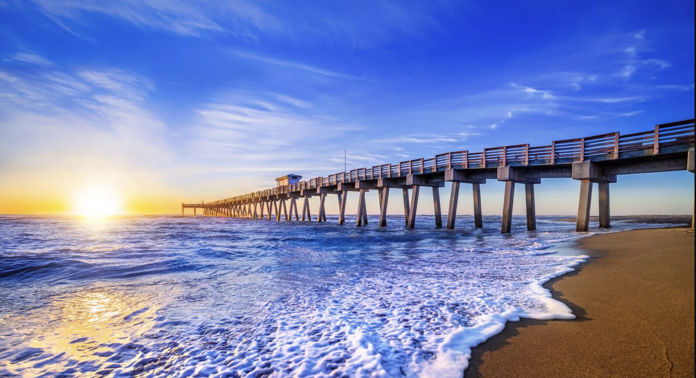 Sunset over the ocean with Venice Florida pier extending into the water, waves crashing onto the sandy beach, under a blue sky with clouds. Near Sharky's restaurant. Beach Wedding.
