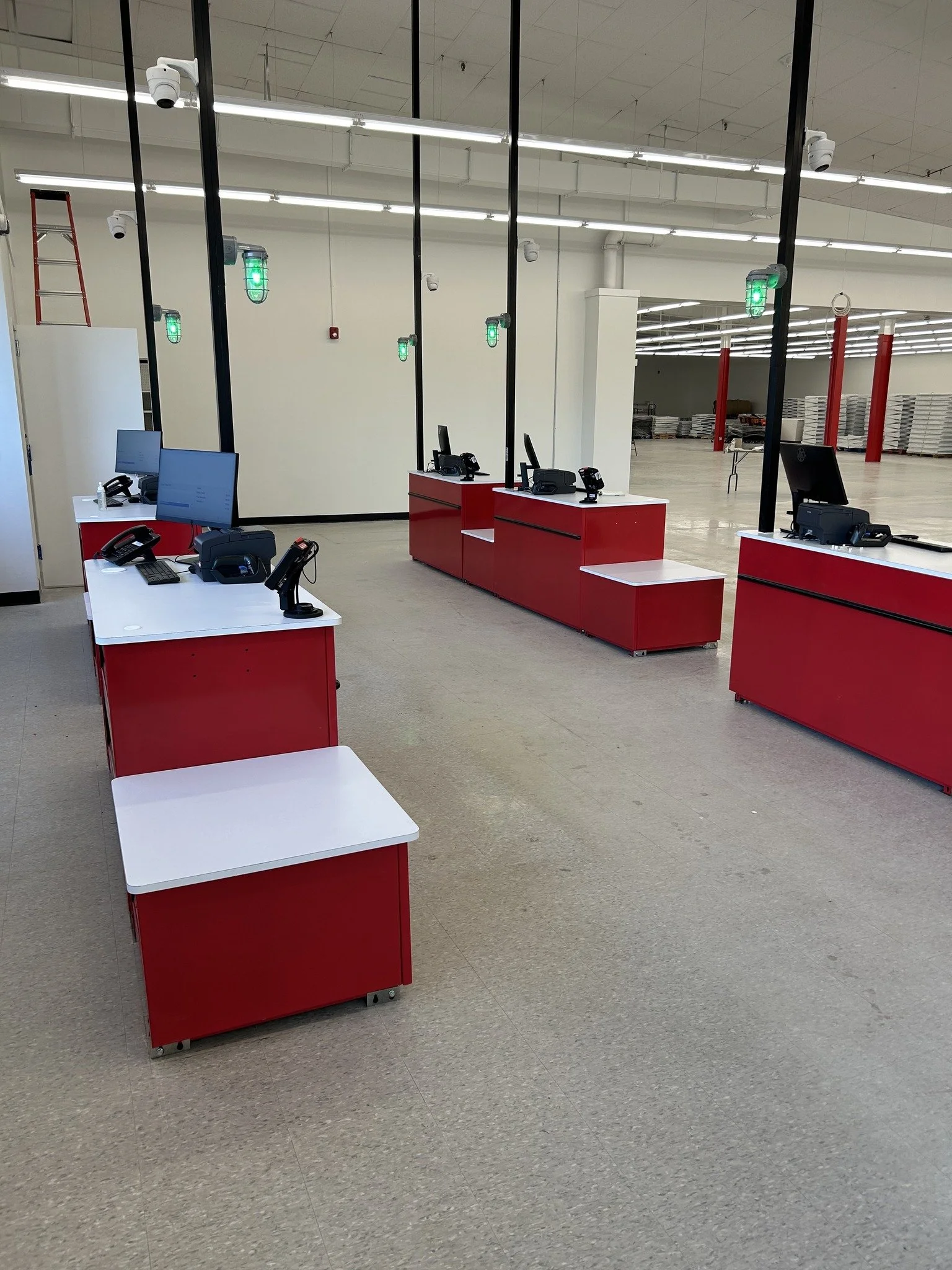 Empty checkout counters with red and white fronts, black poles with green lights, and monitors in an unfinished retail store
