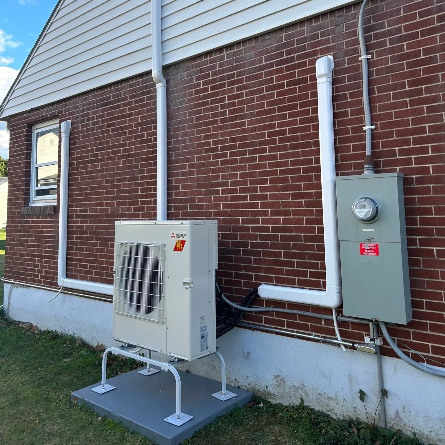 Exterior view of a house showcasing an HVAC unit and electrical meter box installed on a brick wall.
