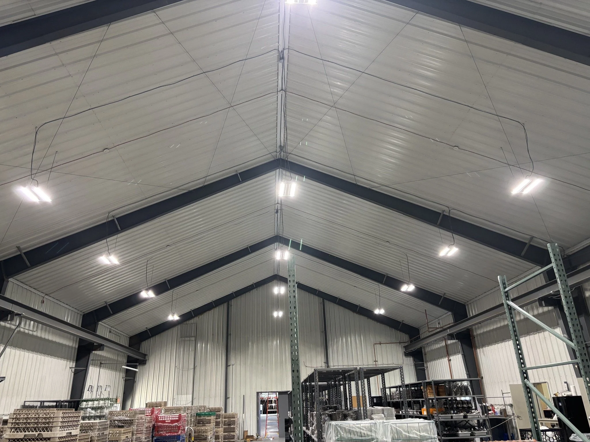 Interior view of a warehouse with high metal ceiling, metal shelving units, and stacked pallets.