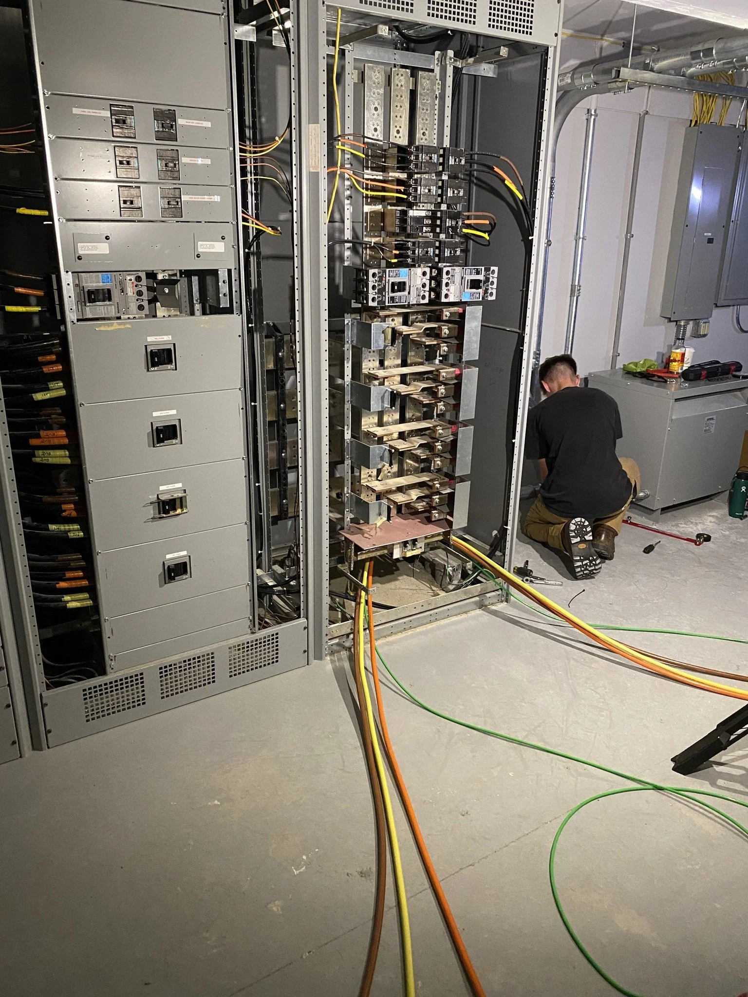Technician working inside an electrical panel with various wires and circuit breakers, in an industrial setting.