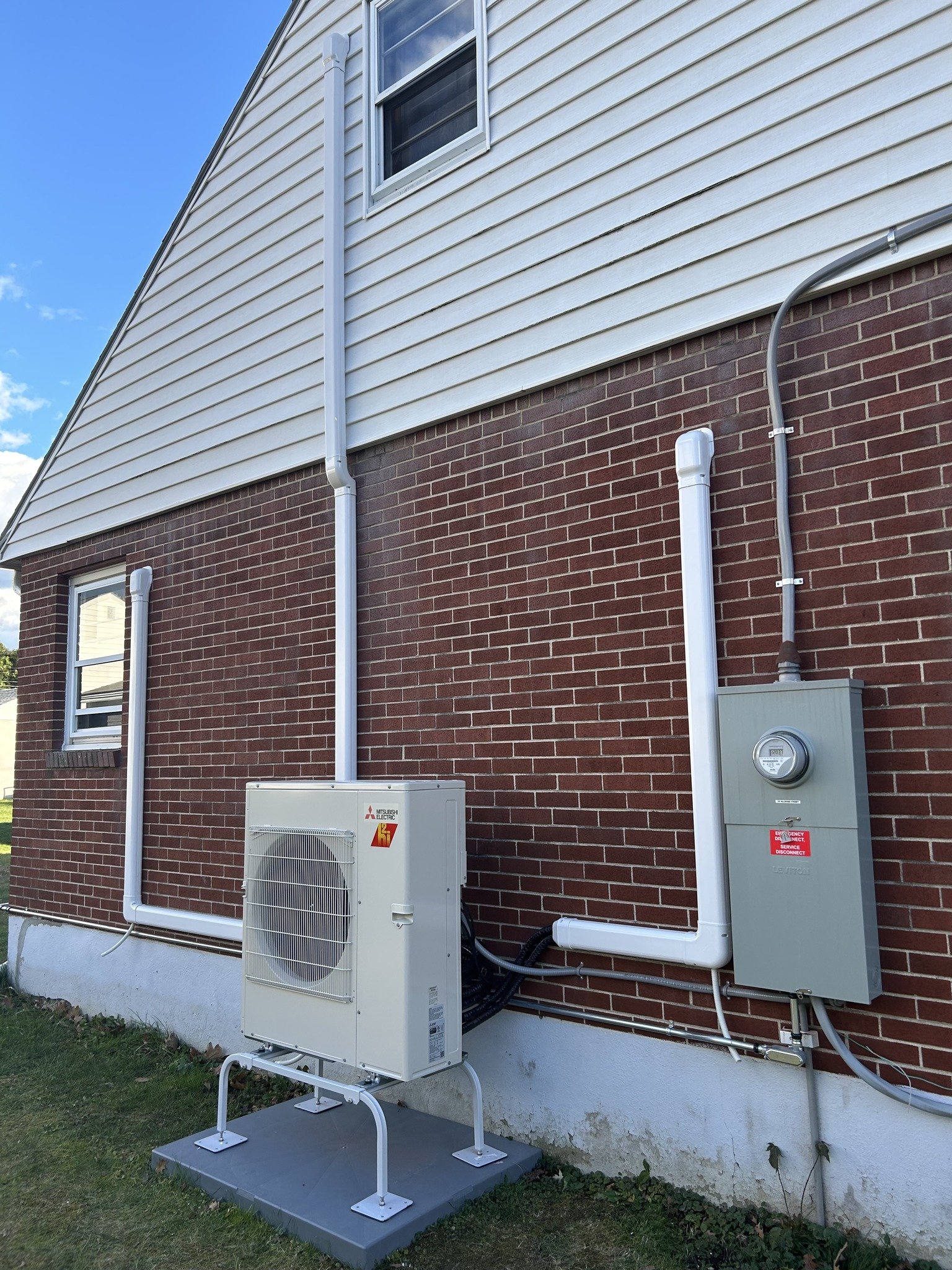Exterior view of a house showing HVAC equipment and electrical wiring on the brick wall.